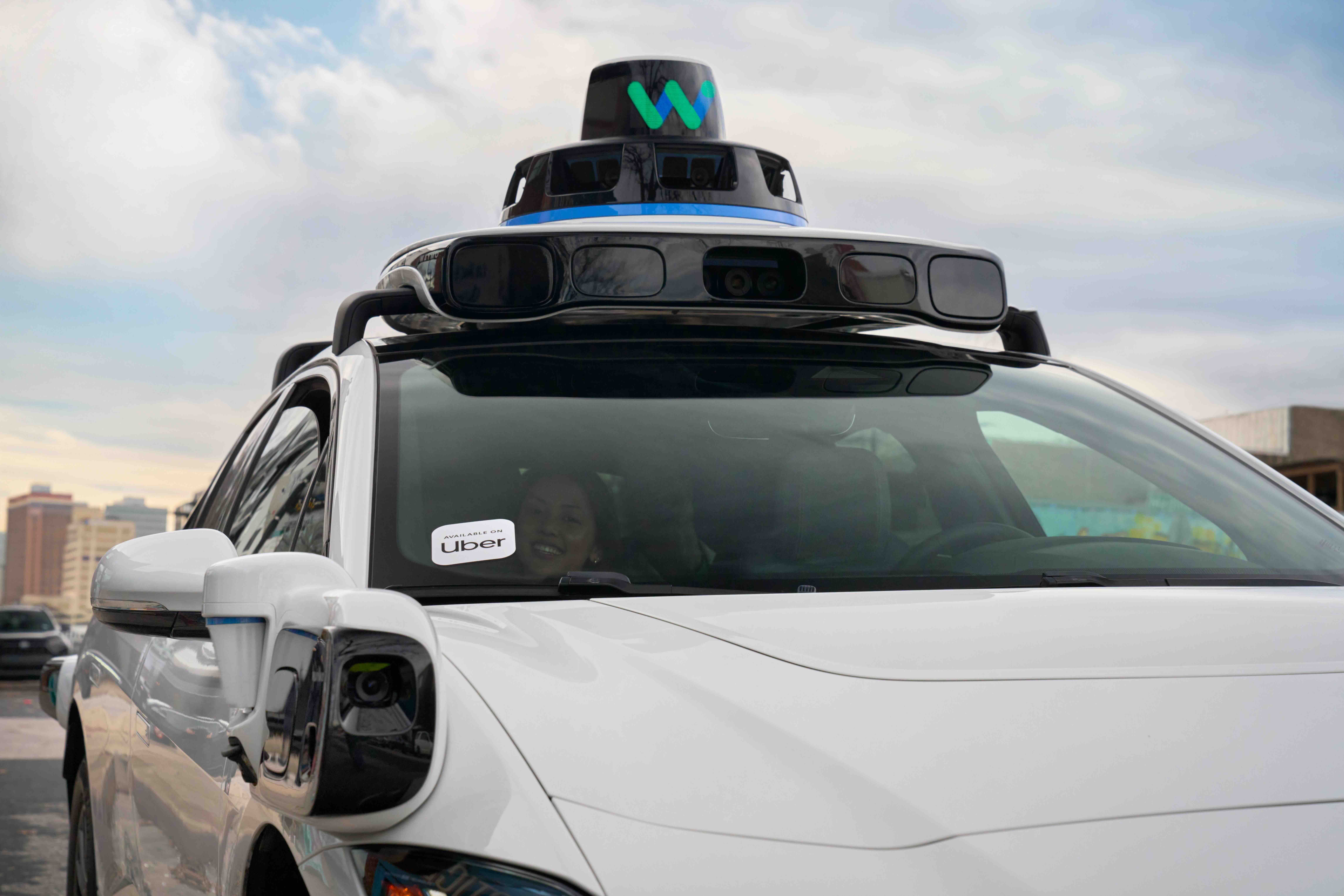A photo of a person in the front of a Waymo. The car has a sticker on the windshield that reads "Uber."