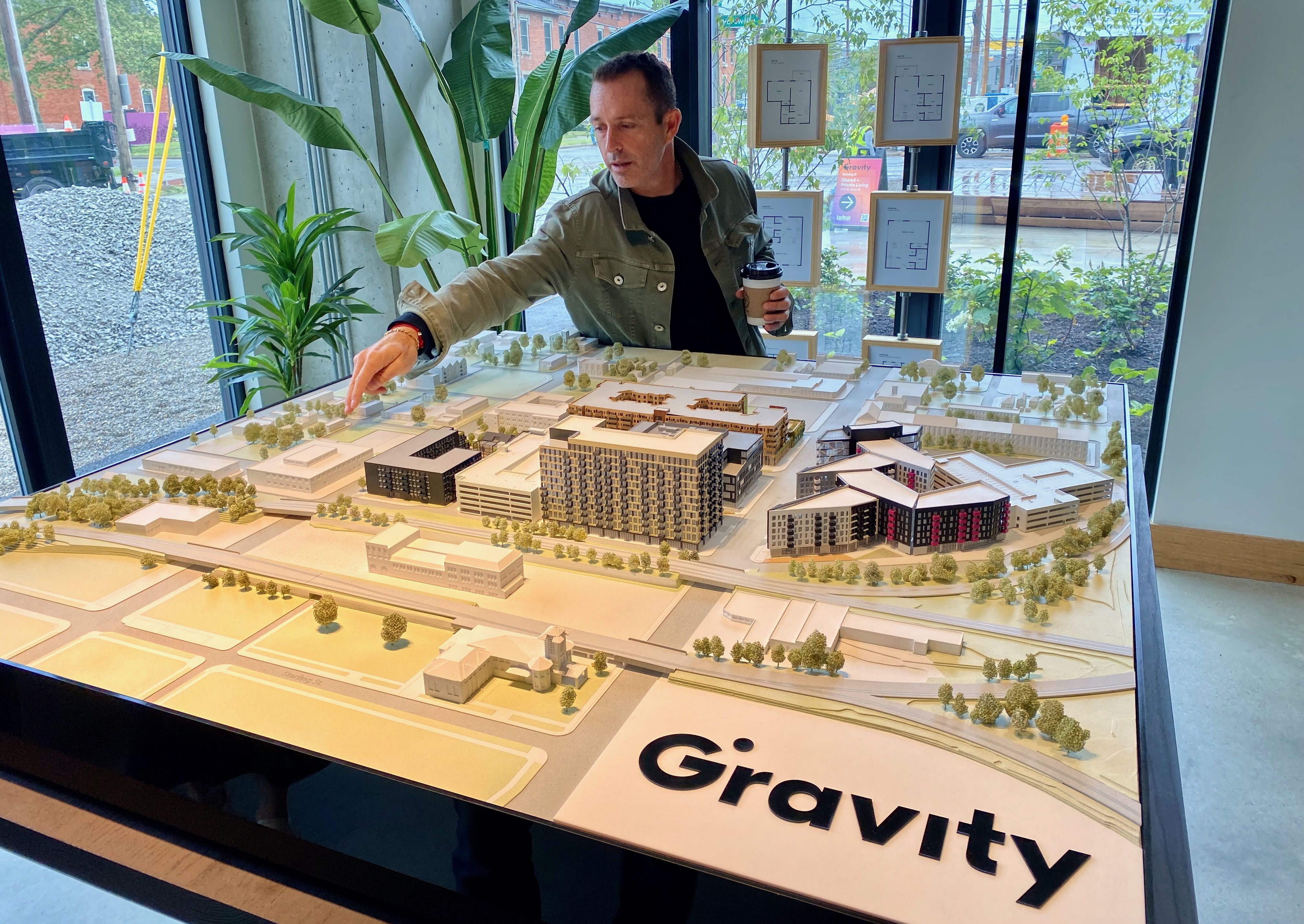 Brett Kaufman stands pointing over a model of the Gravity development project