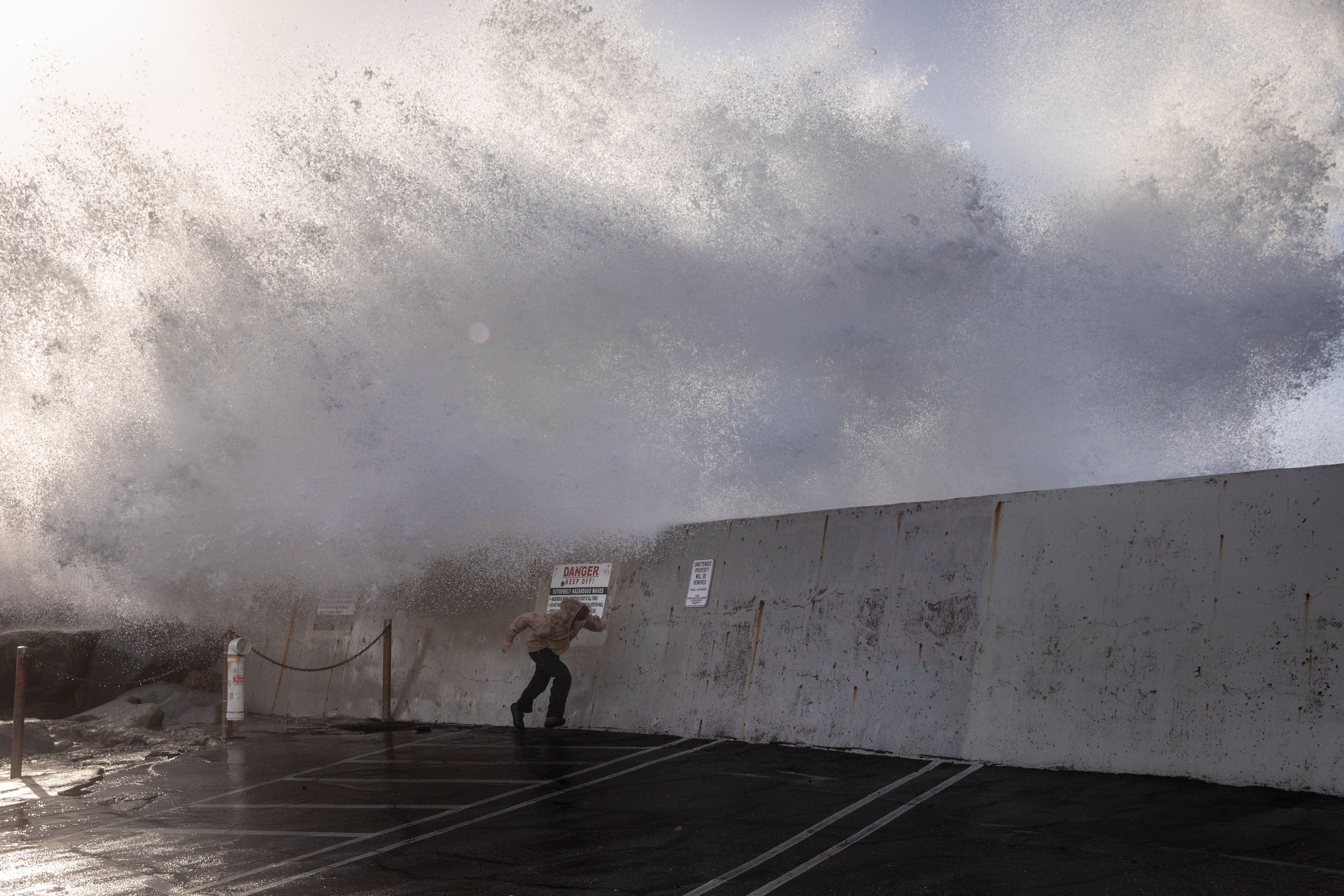 A yman runs from the spray of waves hitting and going over the breakwall of Redondo Beach, CA, Harbor, in the wake of a storm in Los Angeles County, Thursday, Jan. 5.