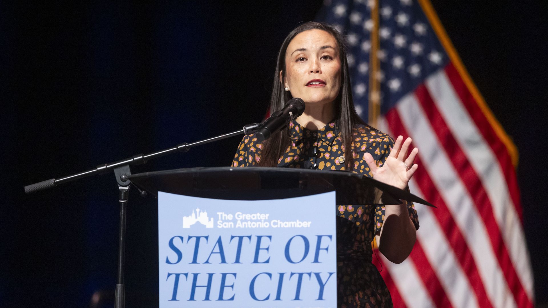 Mayor Gina Ortiz Jones speaks at the State of the City event in April. She is seen standing at a podium in front of a microphone, with her hand in the air. The podium reads "The Greater San Antonio Chamber, State of the City; Building the city of the future."