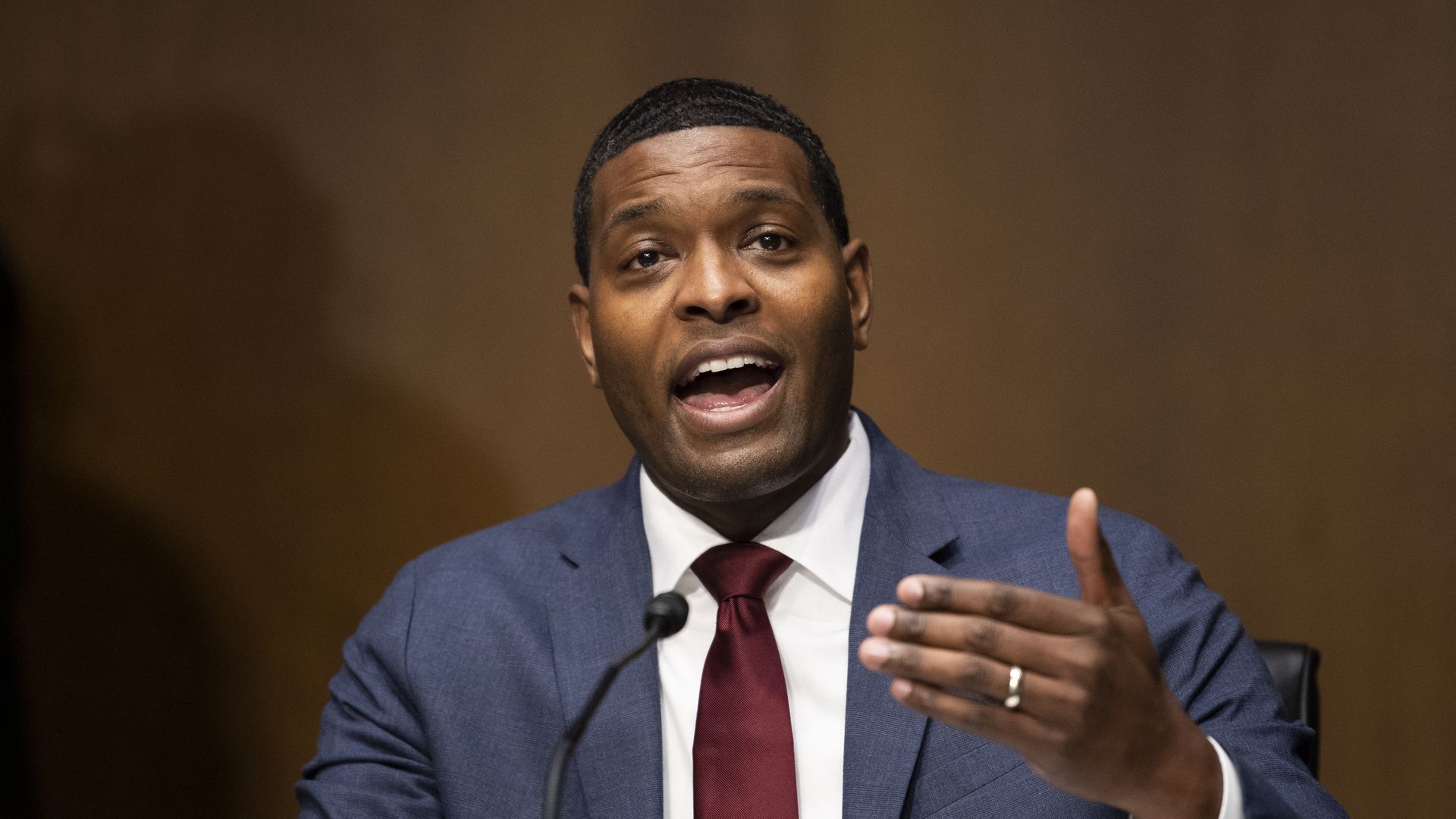 Michael Regan speaks while wearing a red tie and gray suit jacket