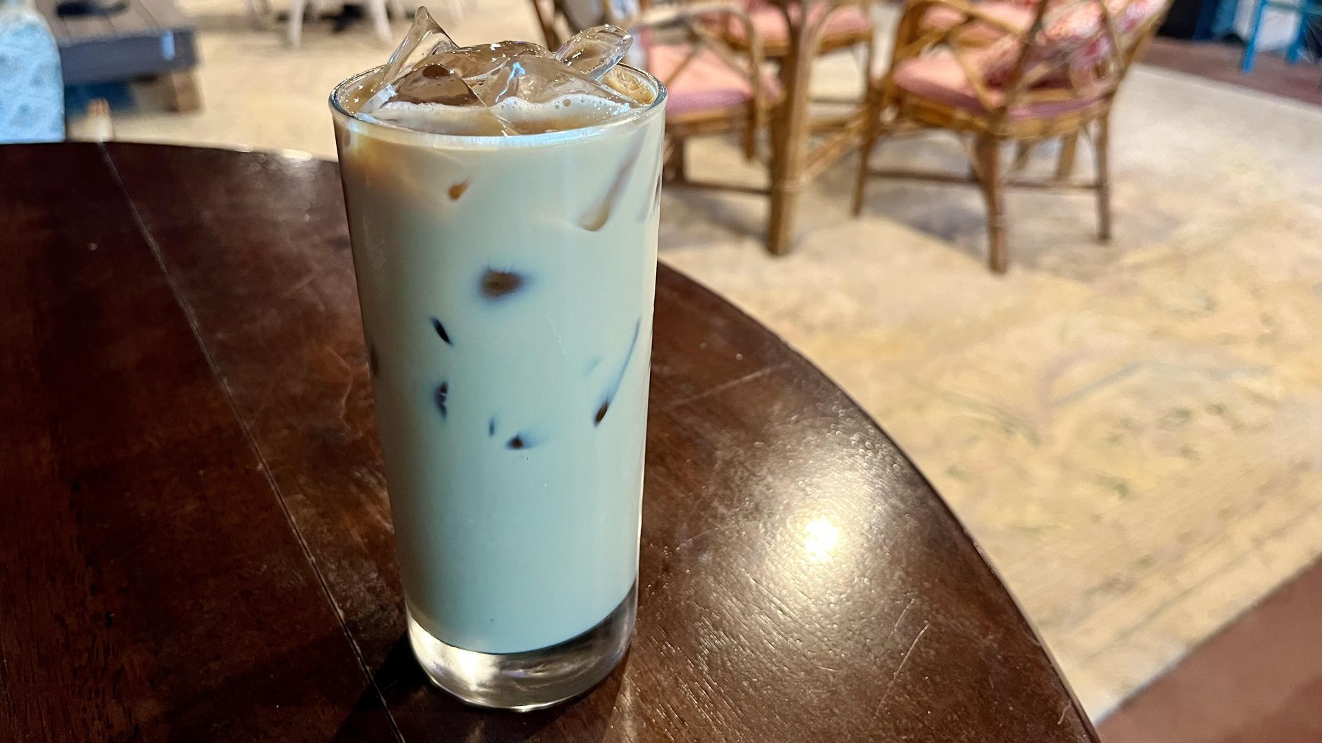 A tall glass holding a light-colored liquid with ice sits on a wooden table.