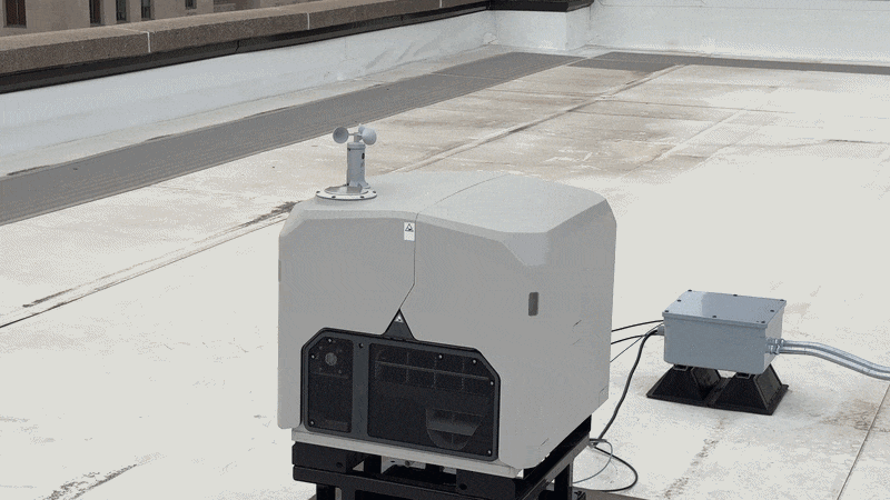 A gray metal box splits open down the middle, opening up to reveal a drone sitting inside with twitching rotors.