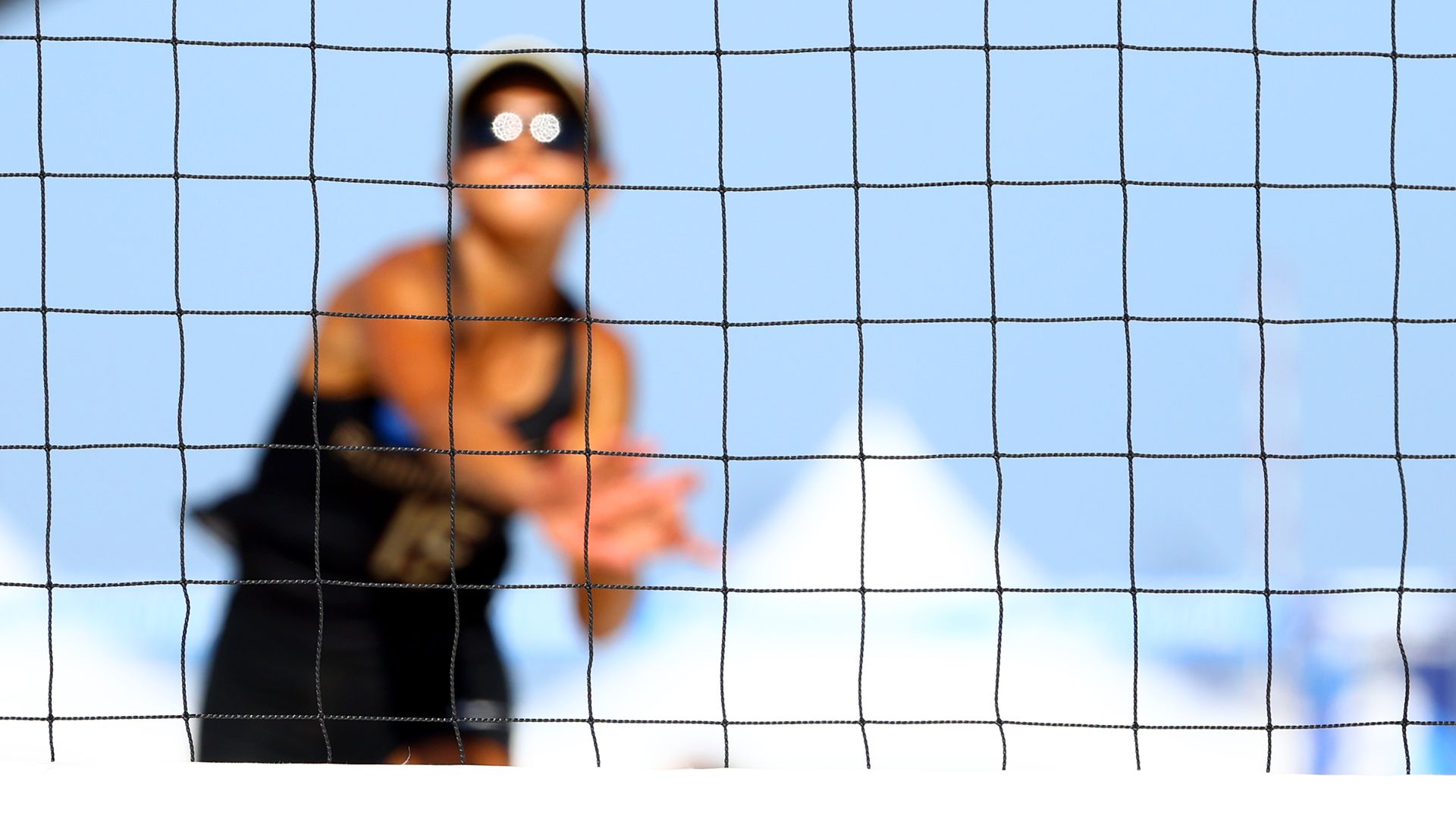 A volleyball player can be seen out of focus in the background, and the net itself is in focus in the foreground. 