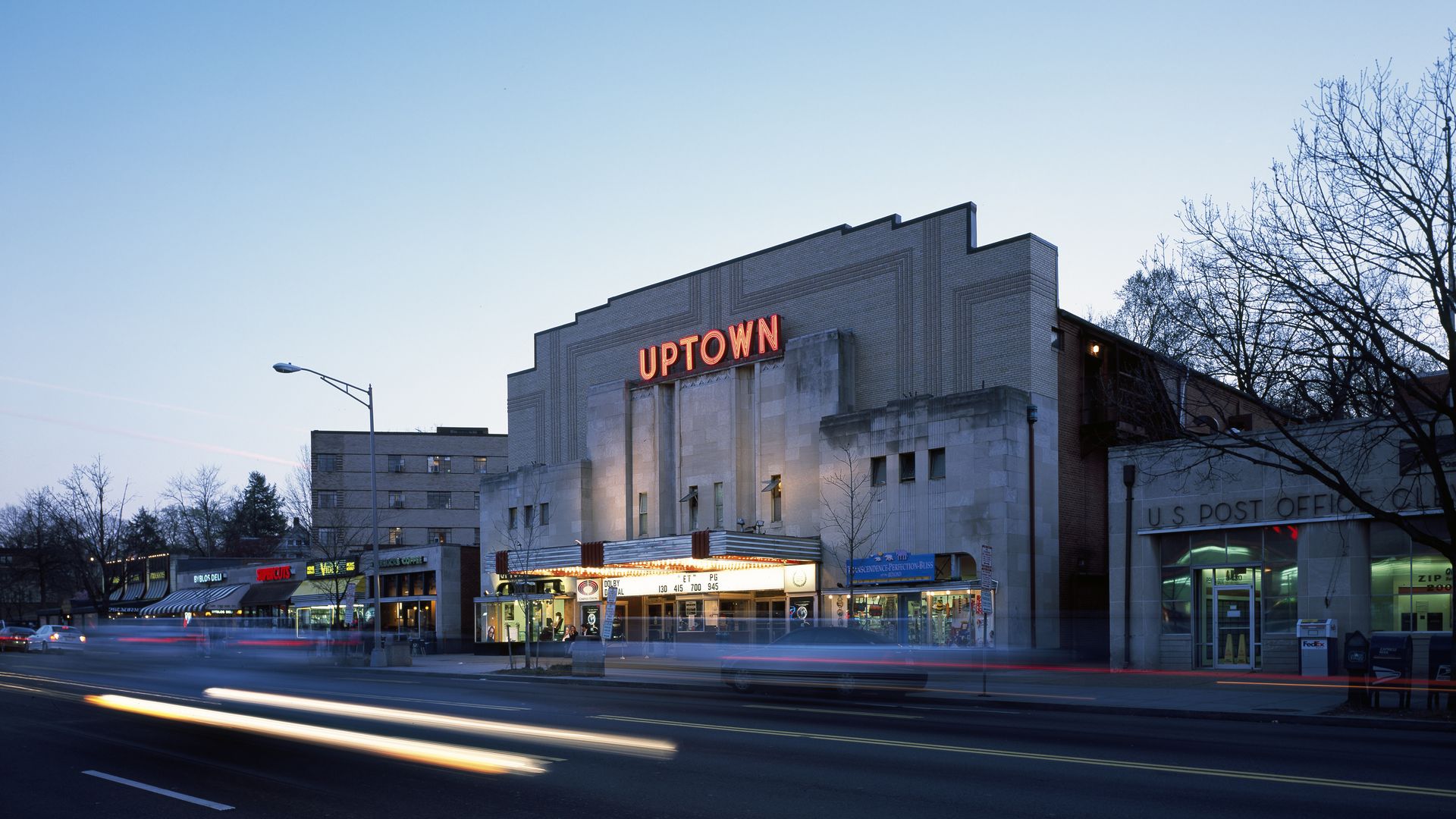 The exterior of Uptown Theater and the neon Uptown sign at dusk, as car lights zip by.