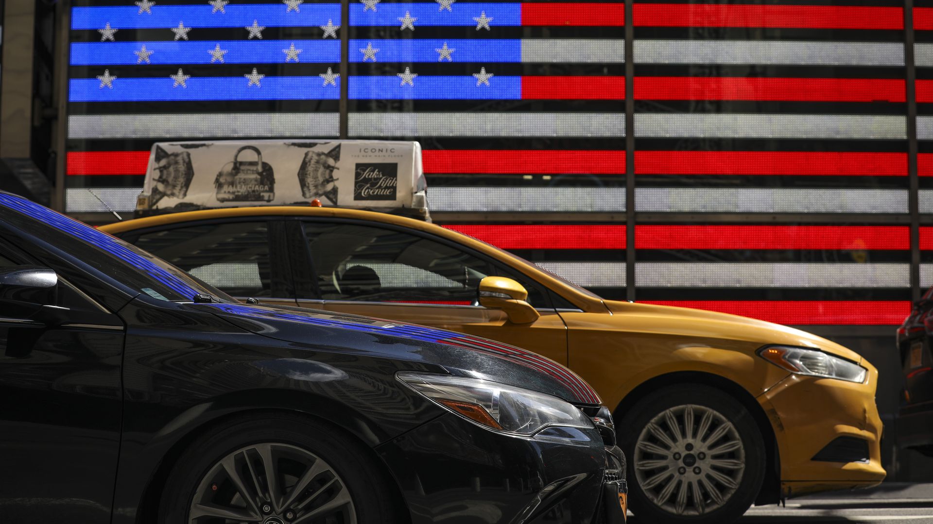 Two cars on the road, driving by an American flag