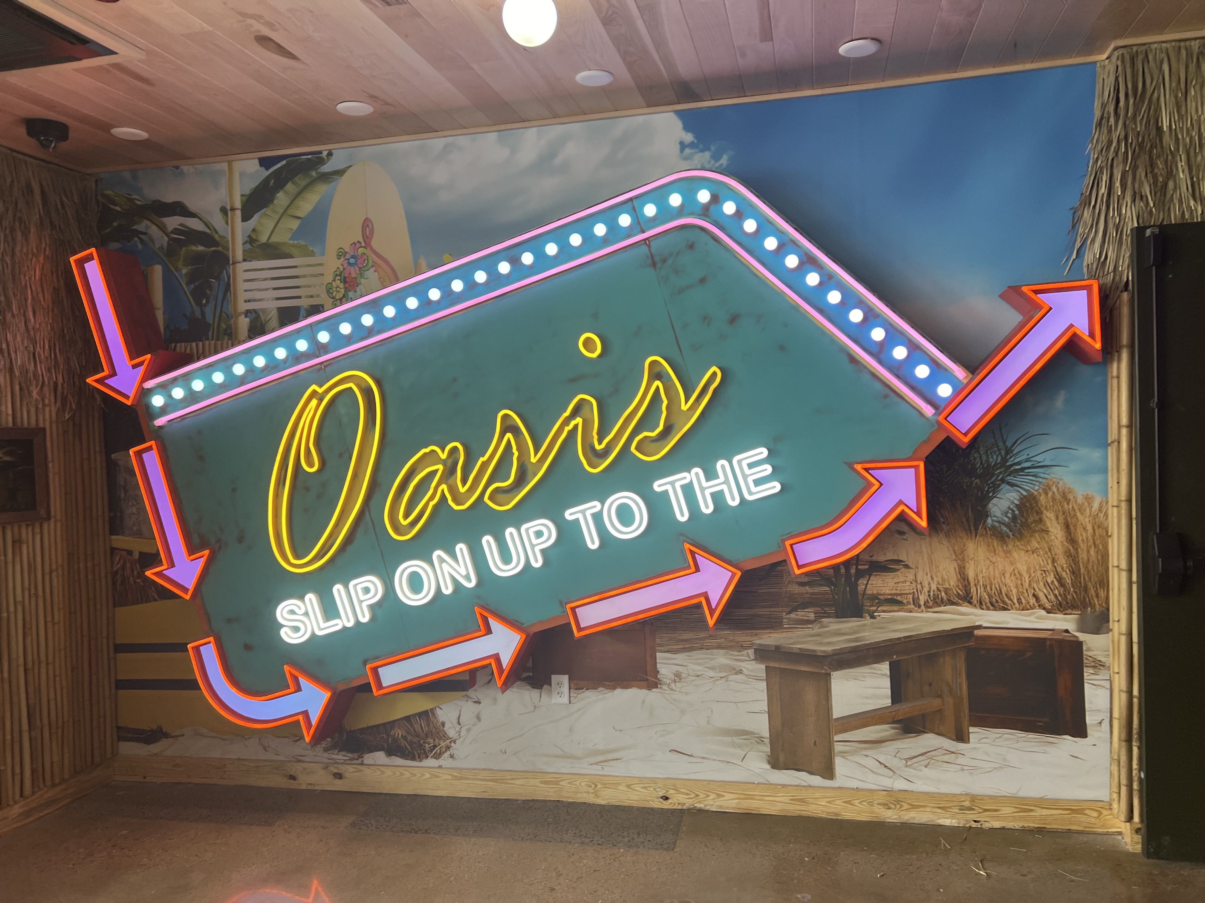 A neon sign that says Slip on up to the Oasis.