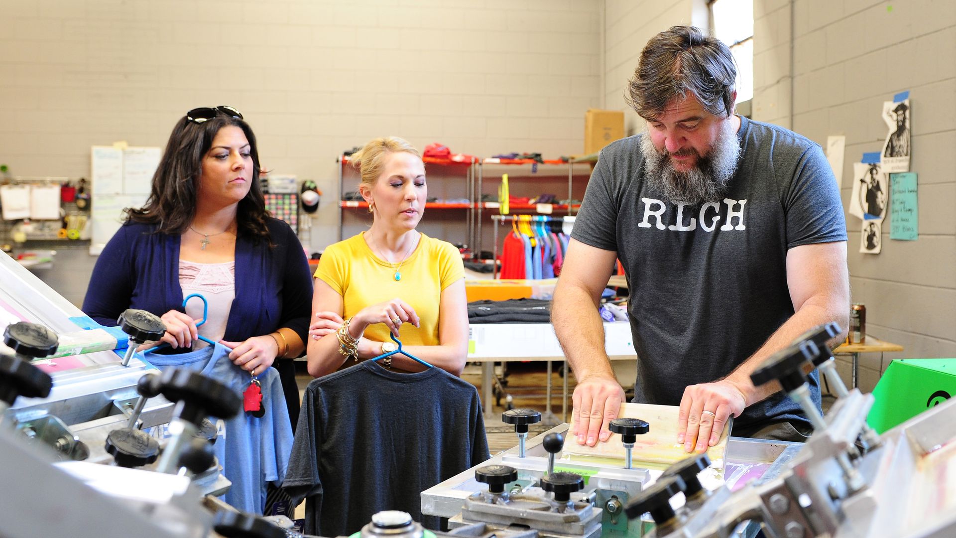 Three people stand around looking at a screen printing machine.