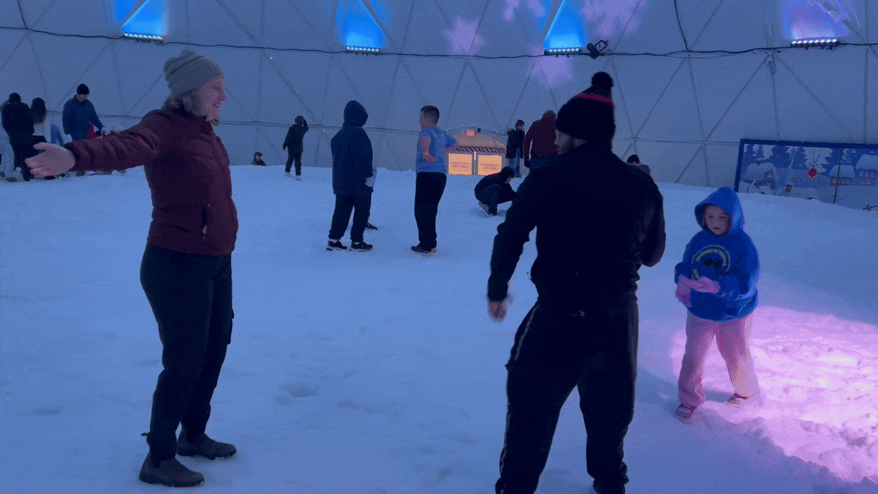 Two adults and two children throwing snowballs inside a snow-covered dome with blue lights. 