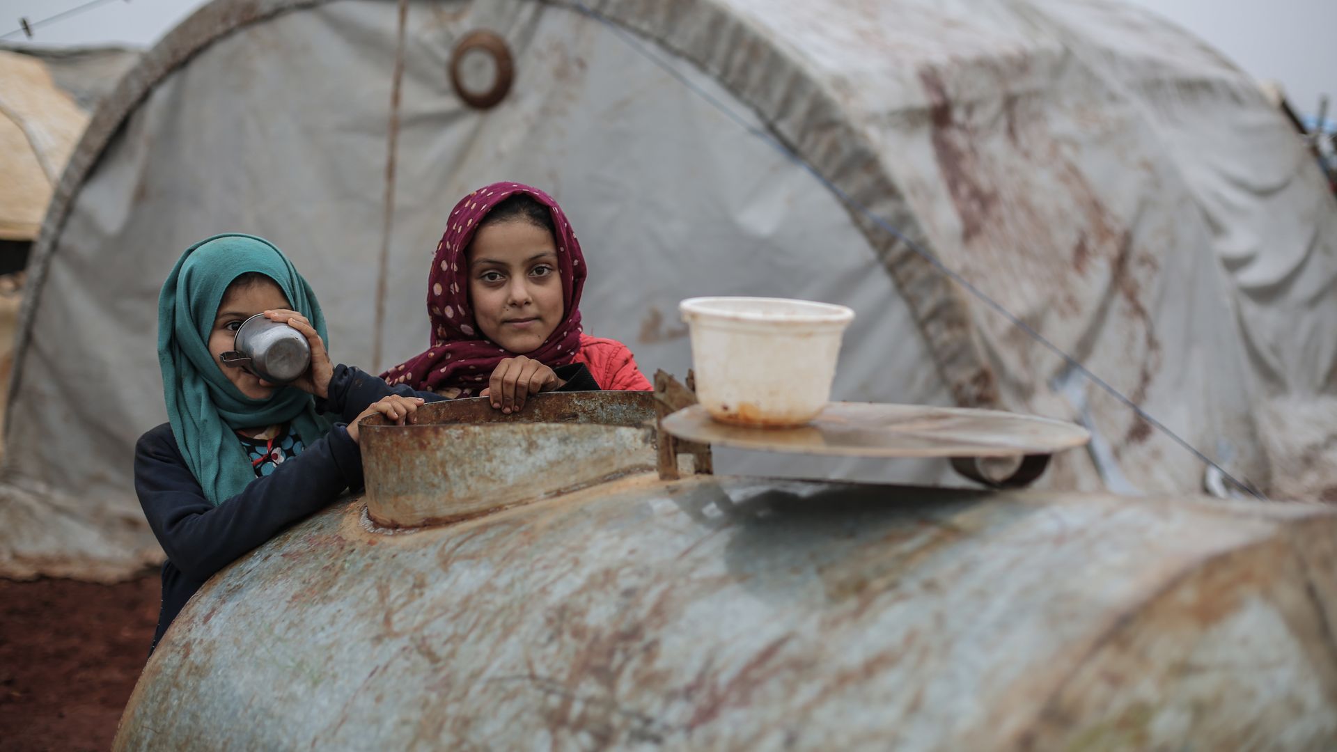 Displaced Syrian girls lean on a cistern during rainy weather at a camp for Syrian displaced people near the Syrian-Turkish border in the Northern countryside of Idlib.