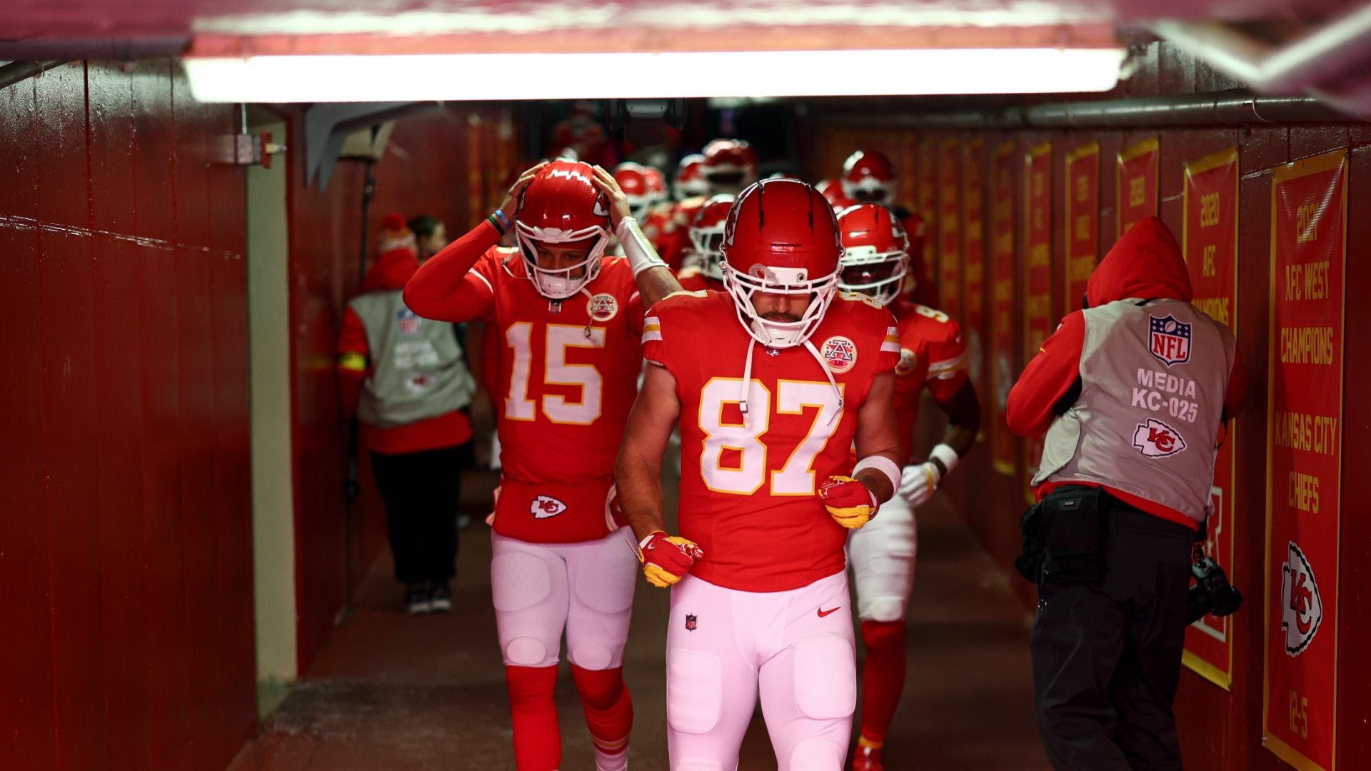 No. 87 Travis Kelce and No. 15 Patrick Mahomes lead the Chiefs in a tunnel wearing red shirted uniforms, helmets and white pants.