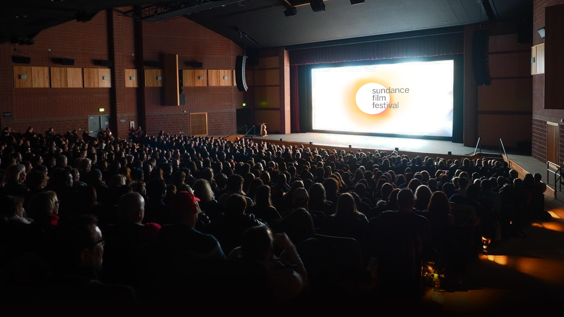 A movie theater full of people with a screen that has "Sundance Film Festival" written.