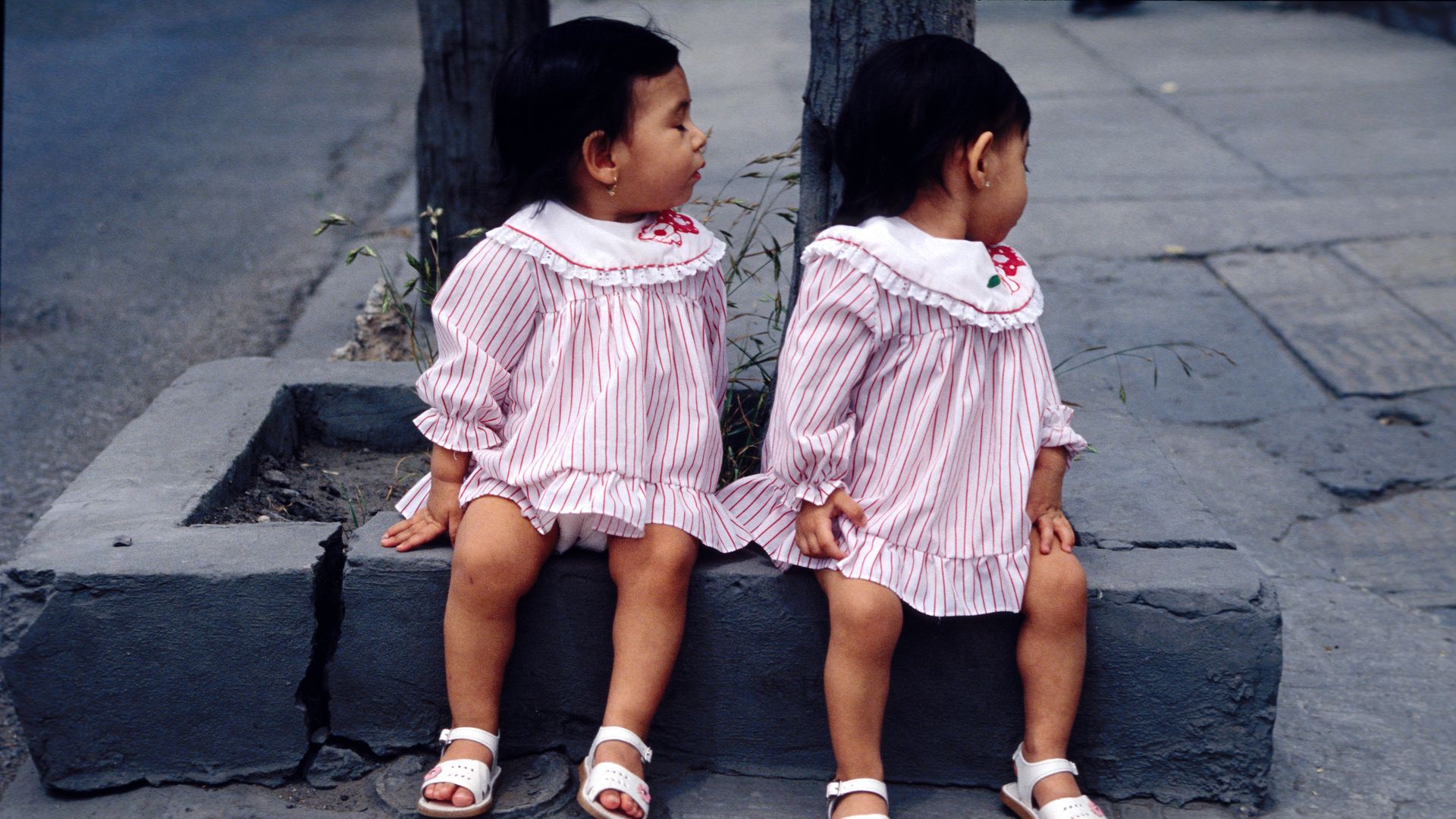 Two girls sitting next to each other in matching pink dresses