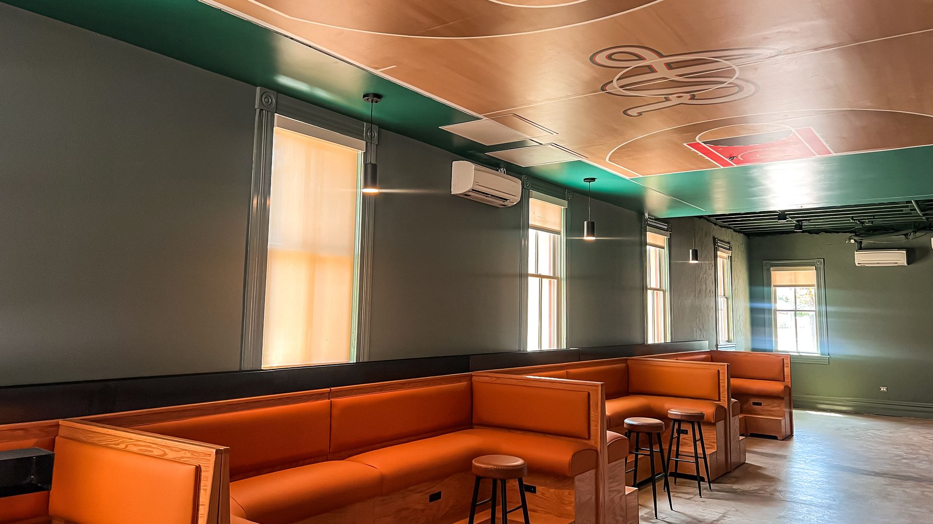 View of an empty bar area with plenty of seating and a painted basketball court on the ceiling. 