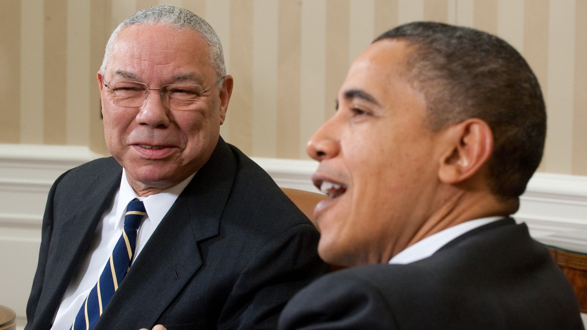 Photo of Colin Powell and Barack Obama sitting together and talking with smiles on their faces