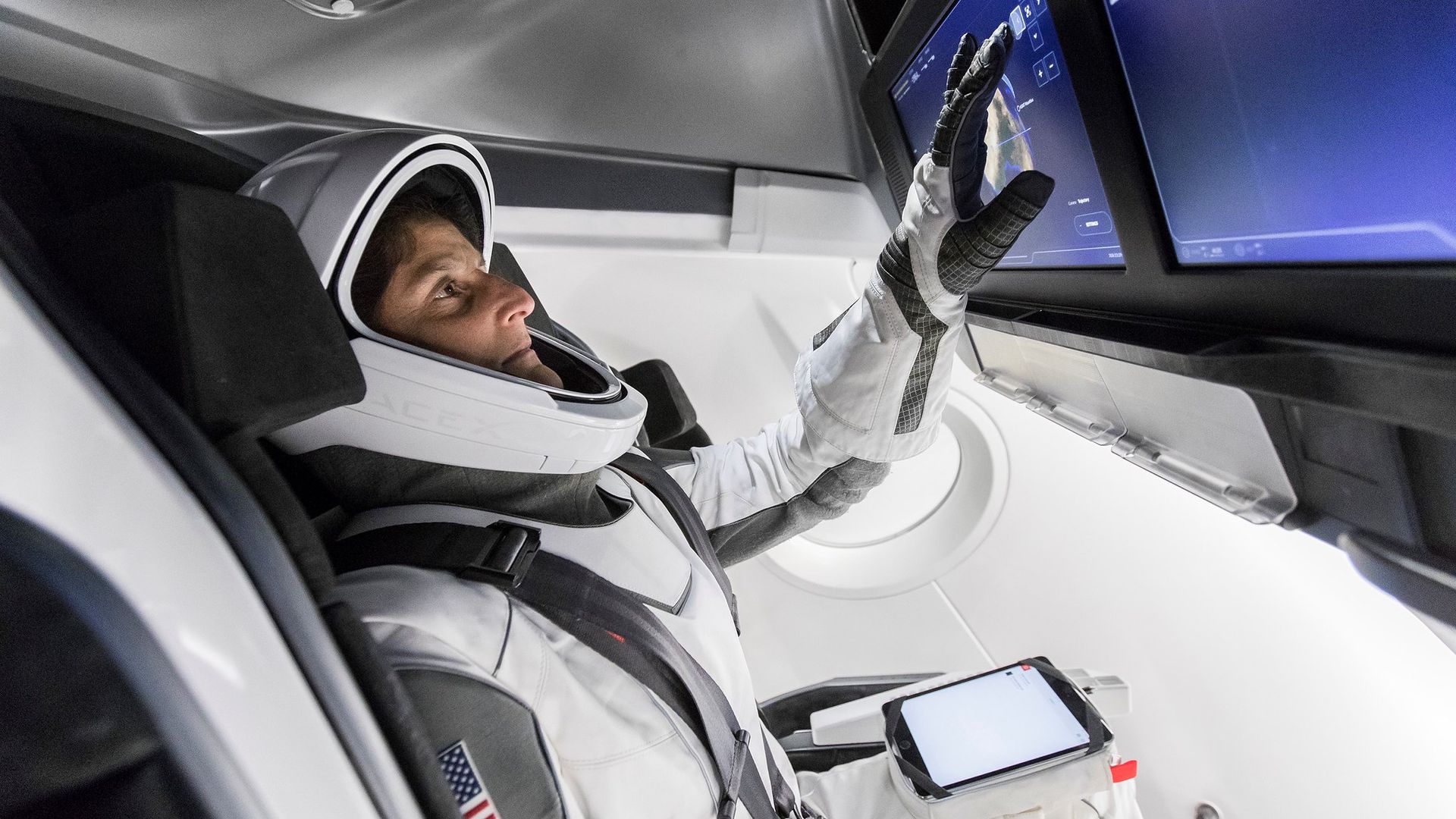 A NASA astronaut wearing a spacesuit touches a screen panel in SpaceX's Dragon capsule