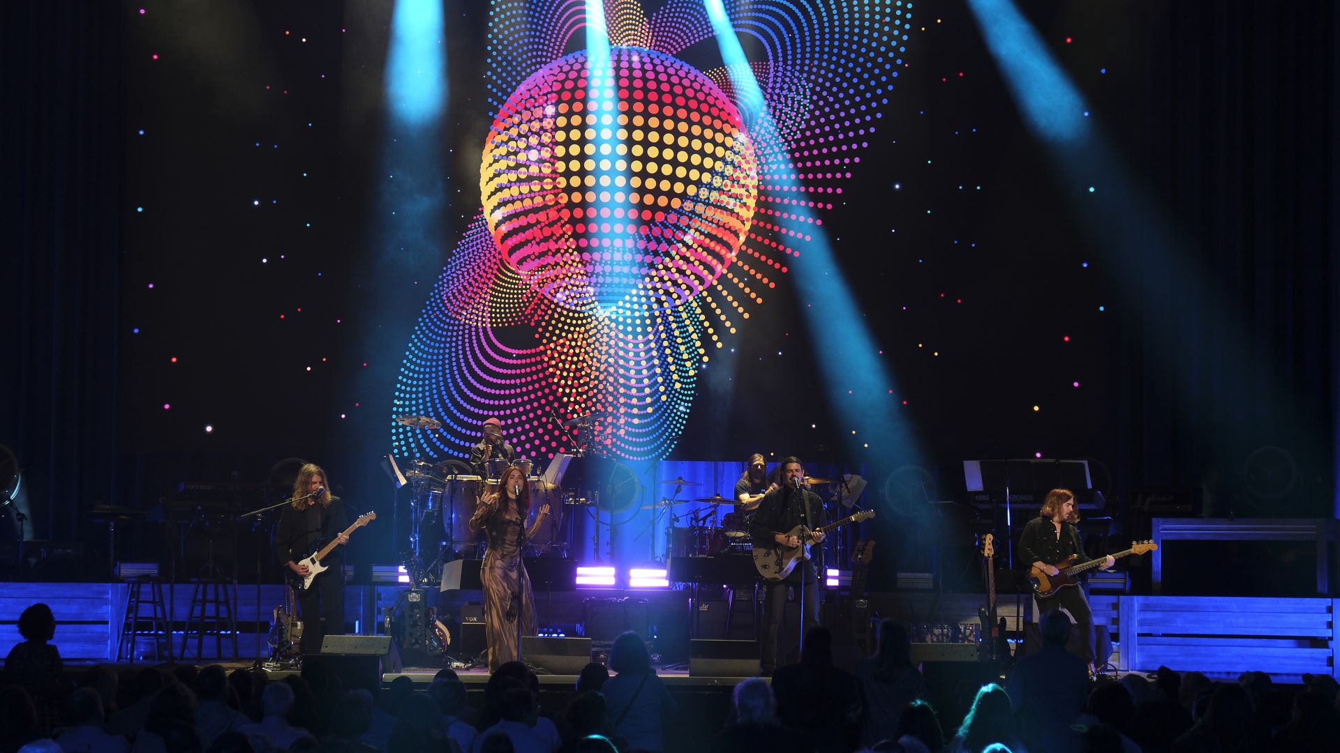A musical group performs on a stage under a multi-colored disco ball