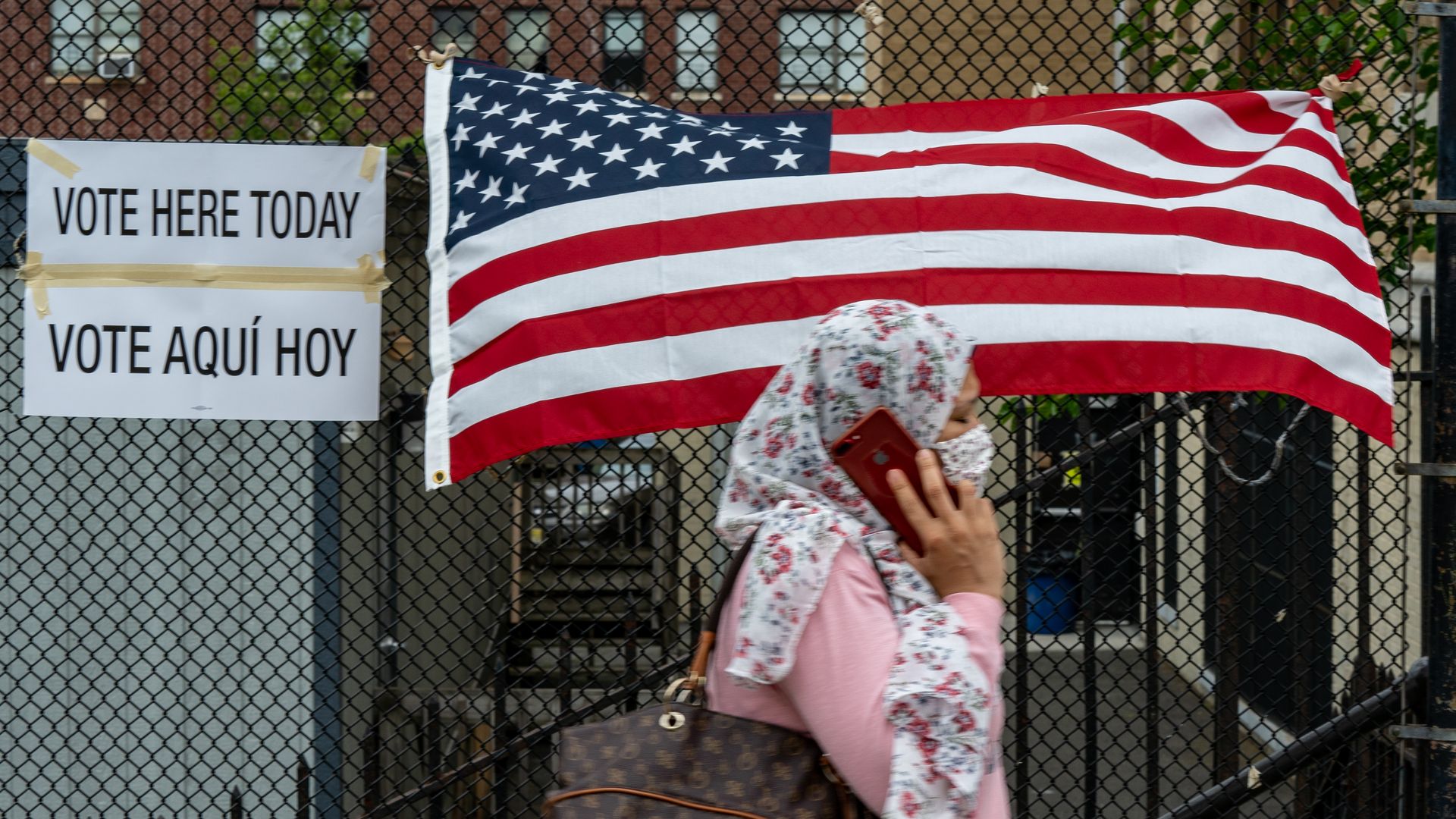 A person walking past an American flag and a voting sign.