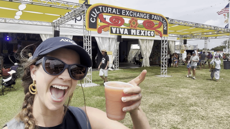 A woman wearing an Axios hat smiles and tips a frozen drink toward the camera.