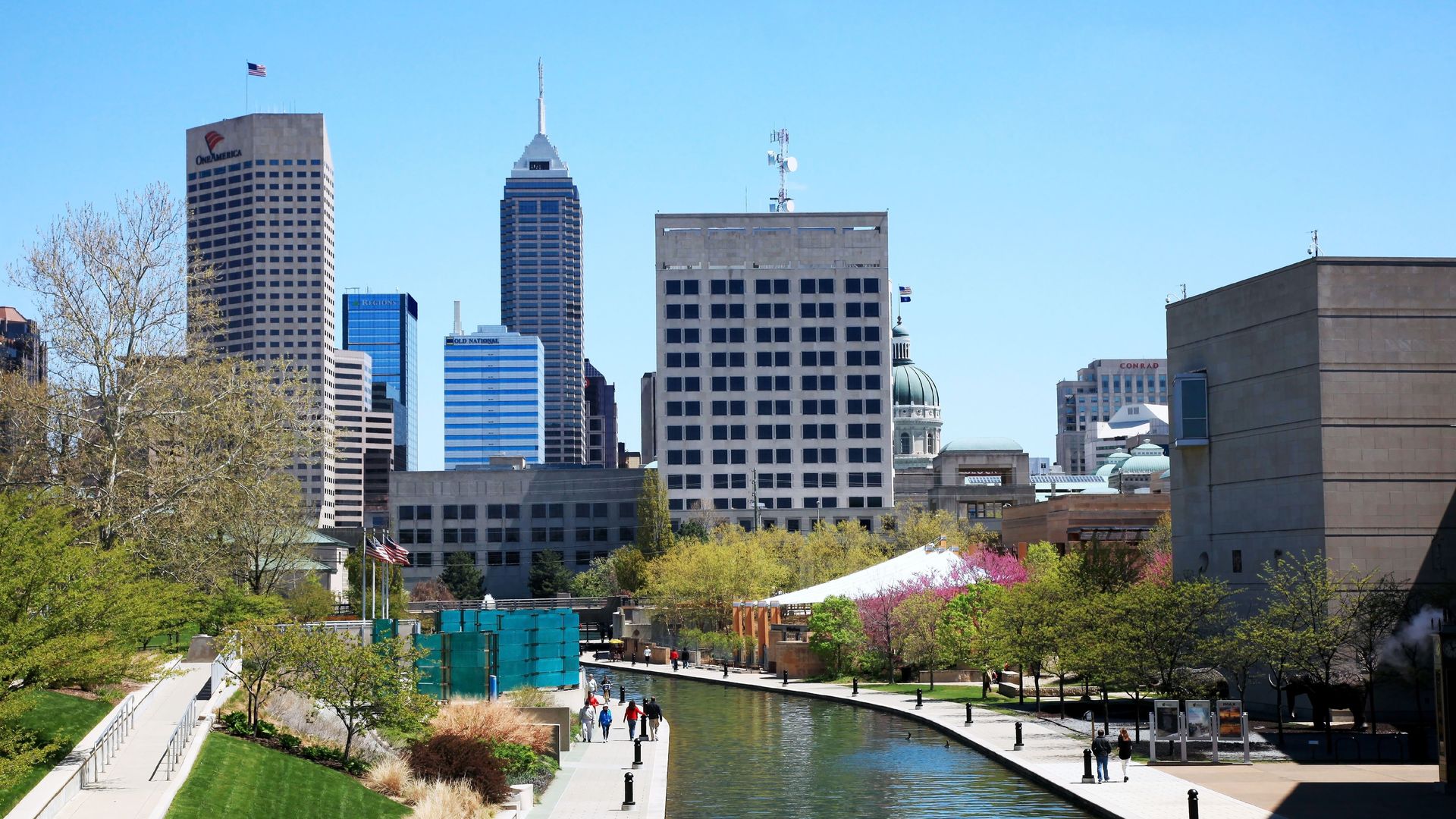 People enjoy a sunny spring day and the city skyline along the Canal Walk in downtown Indianapolis Indiana, The Canal Walk is a large linear park and urban green space associated with White River State Park in the downtown area of the Indiana state capital city of Indianapolis. 