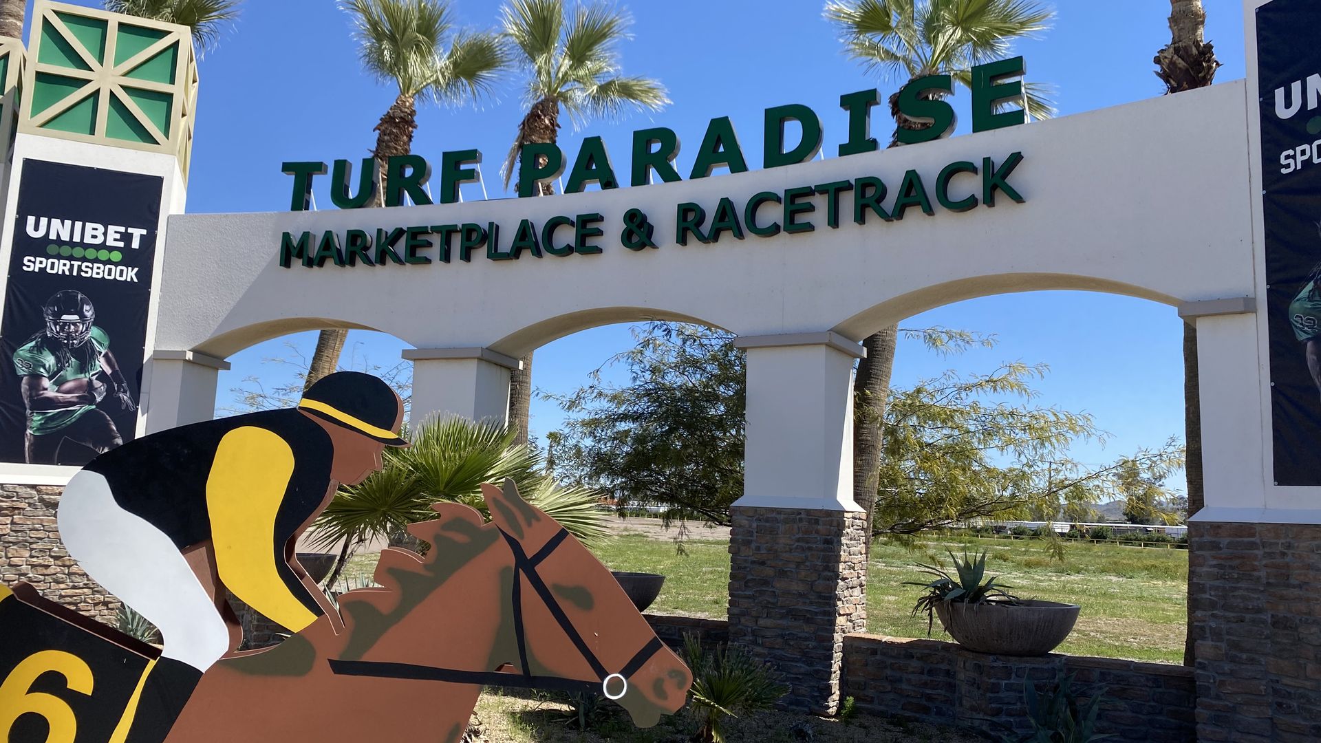 A cutout image of a jockey on a horse in front of a sign reading Turf Paradise marketplace and racetrack.