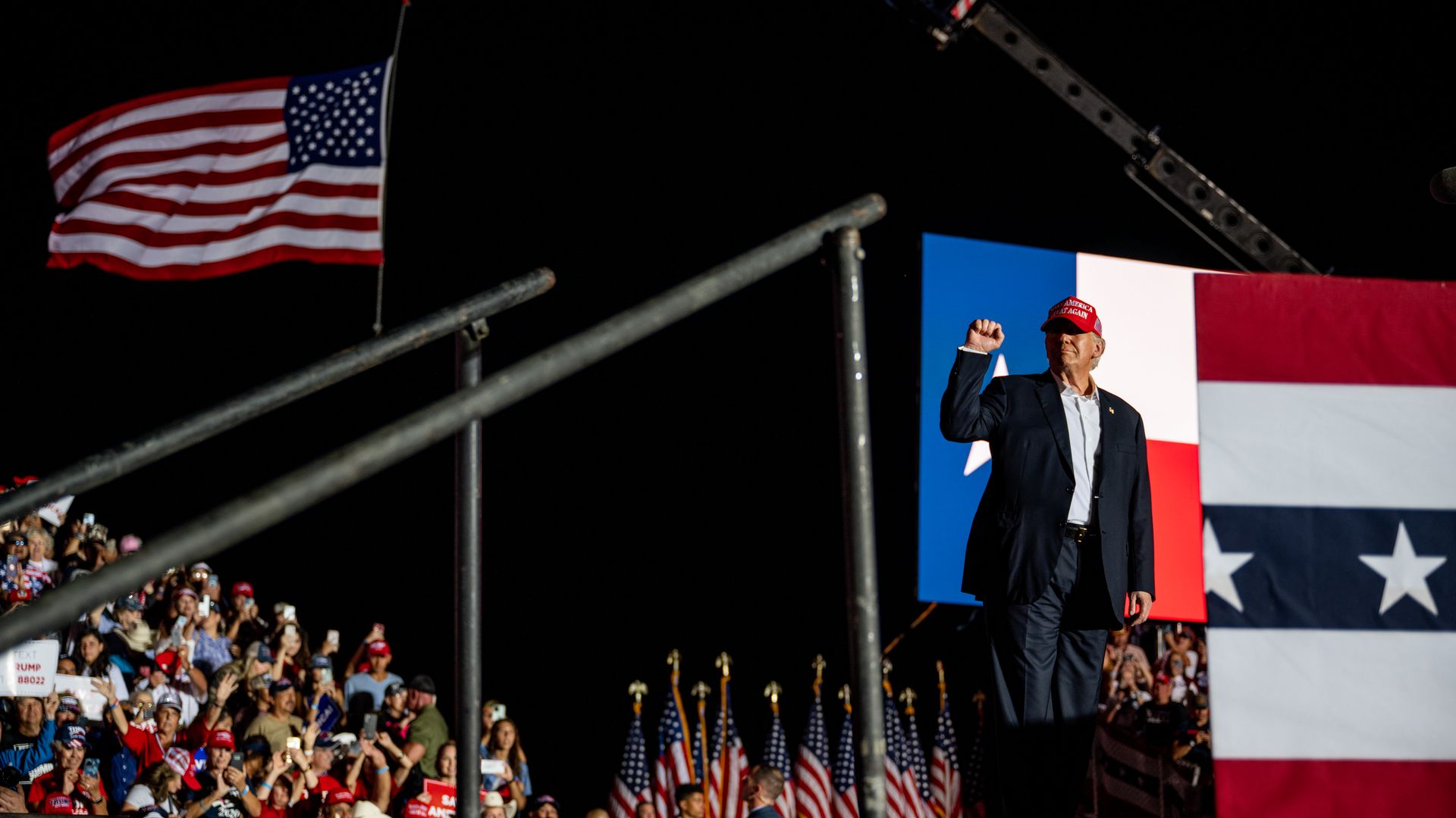 Photo of Donald Trump on a stage, with the American flag behind him at a rally. 