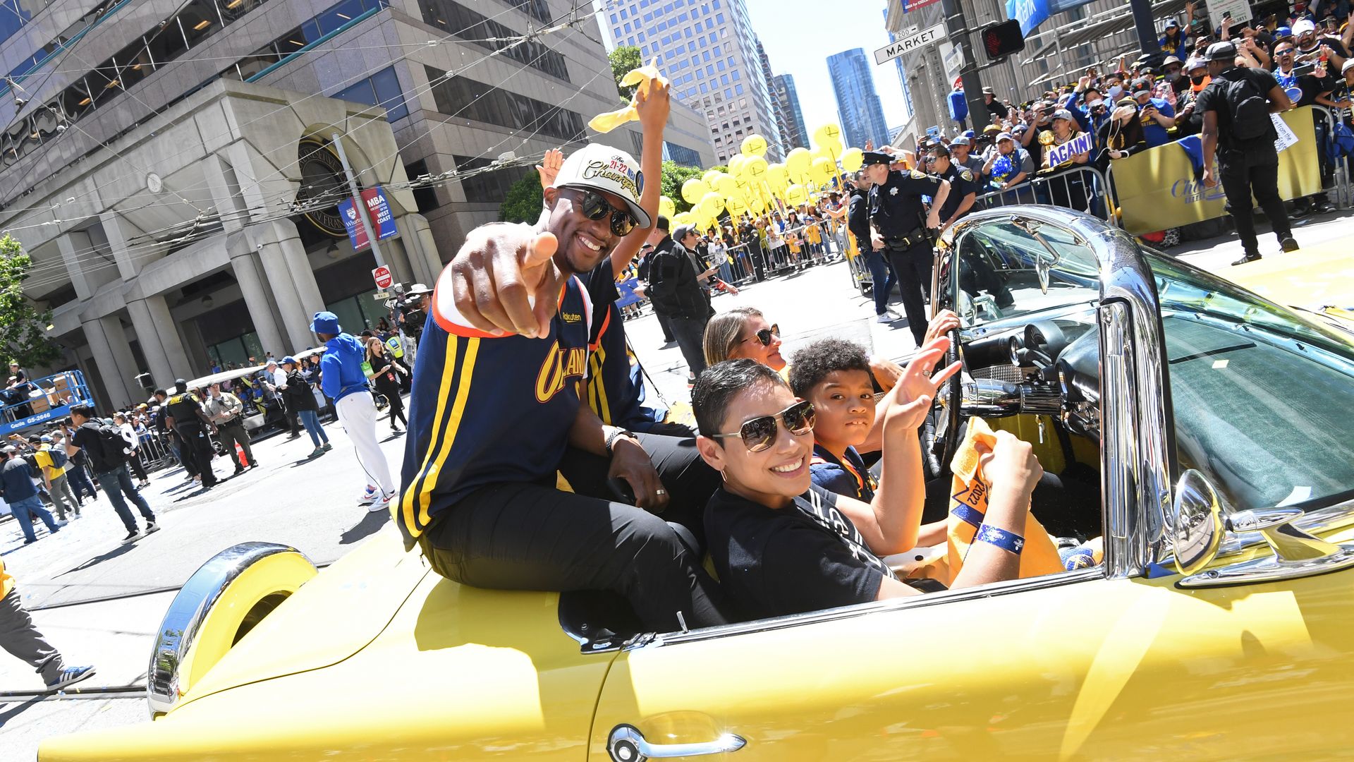 A yellow convertible with its top down, full of people, smiling.