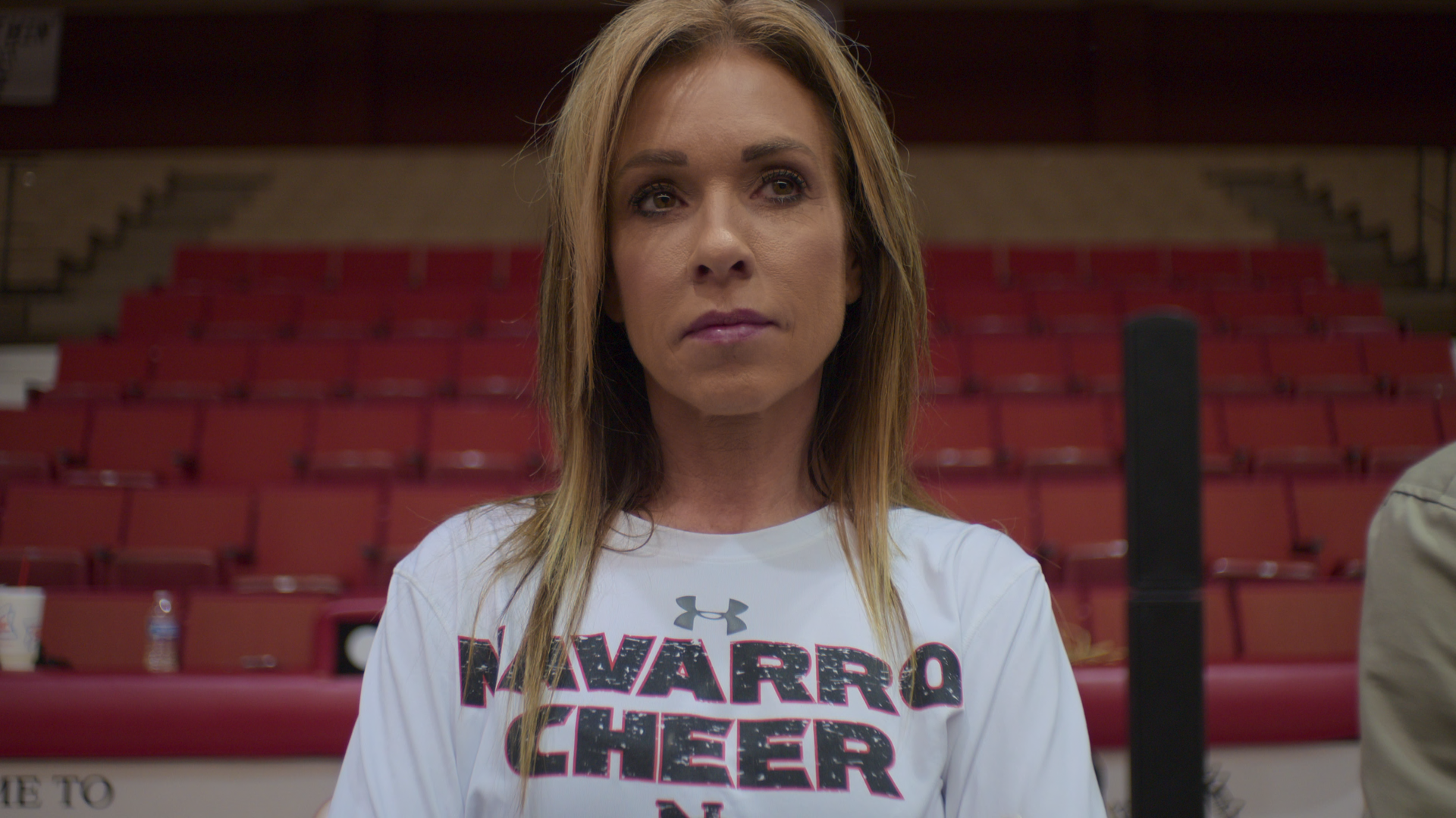 A woman wearing a "NAVARRO CHEER" shirt standing in front of bleachers