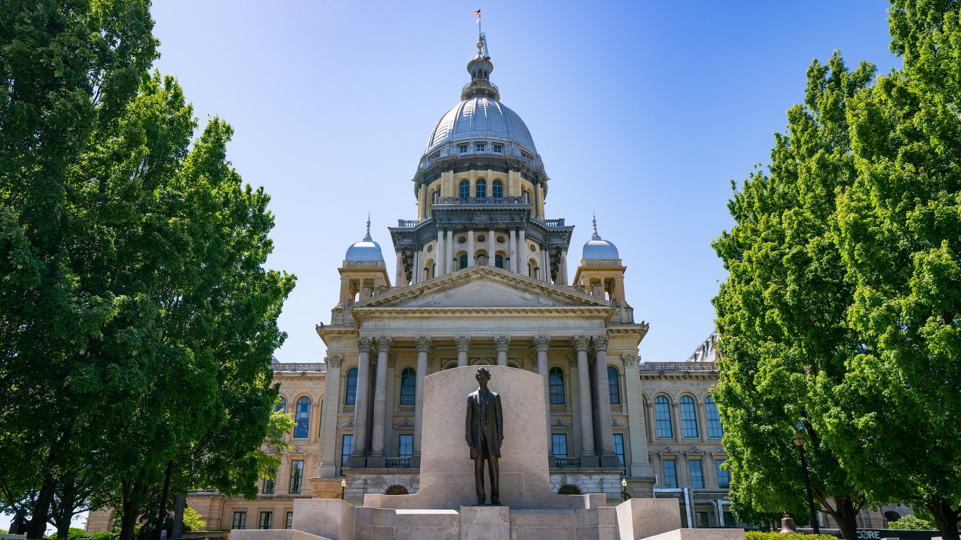 The Illinois State Capitol Building, featuring a statue of Abraham Lincoln at the steps leading to the entrance of the capitol.