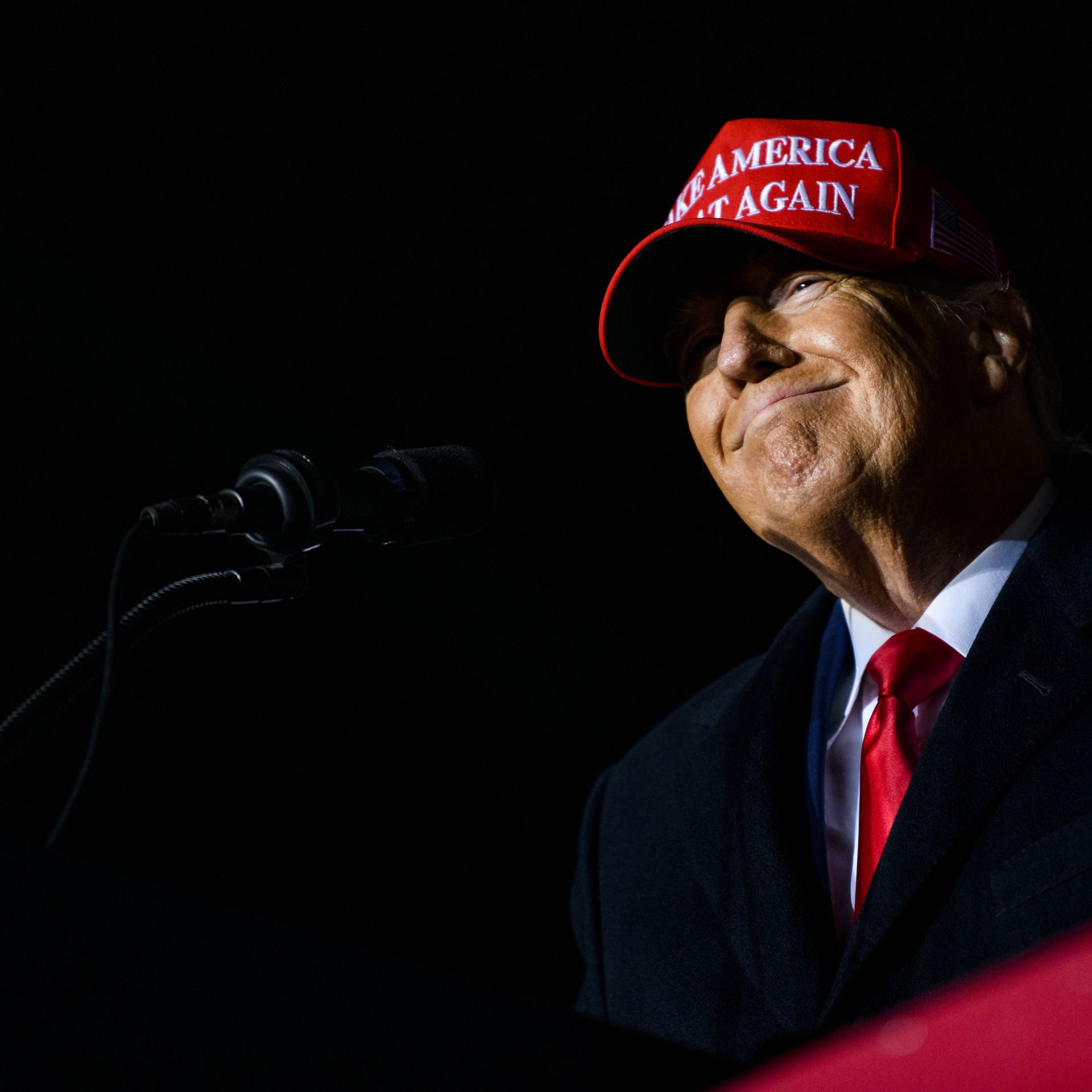 President Trump smiles while wearing a MAGA hat at a rally. 