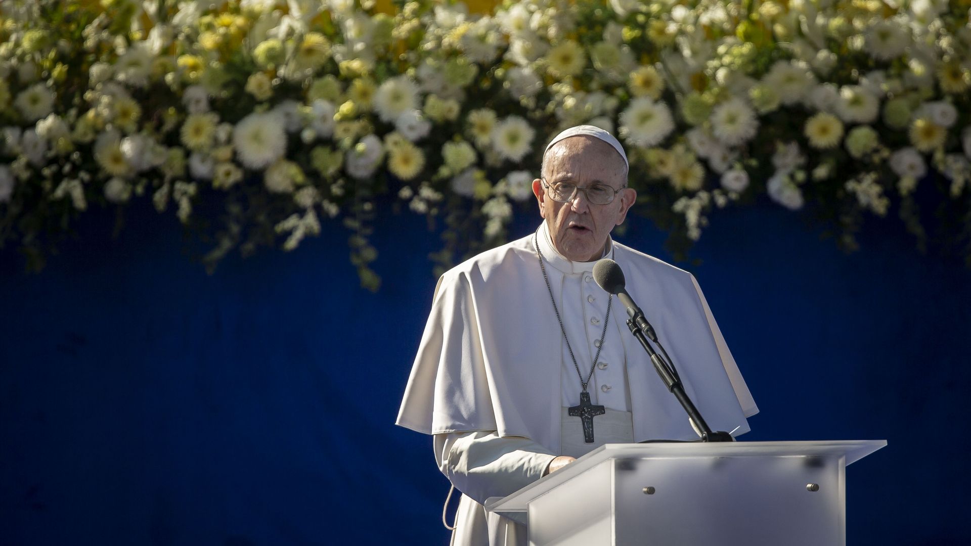 Pope Francis speaks under a banner of flowers