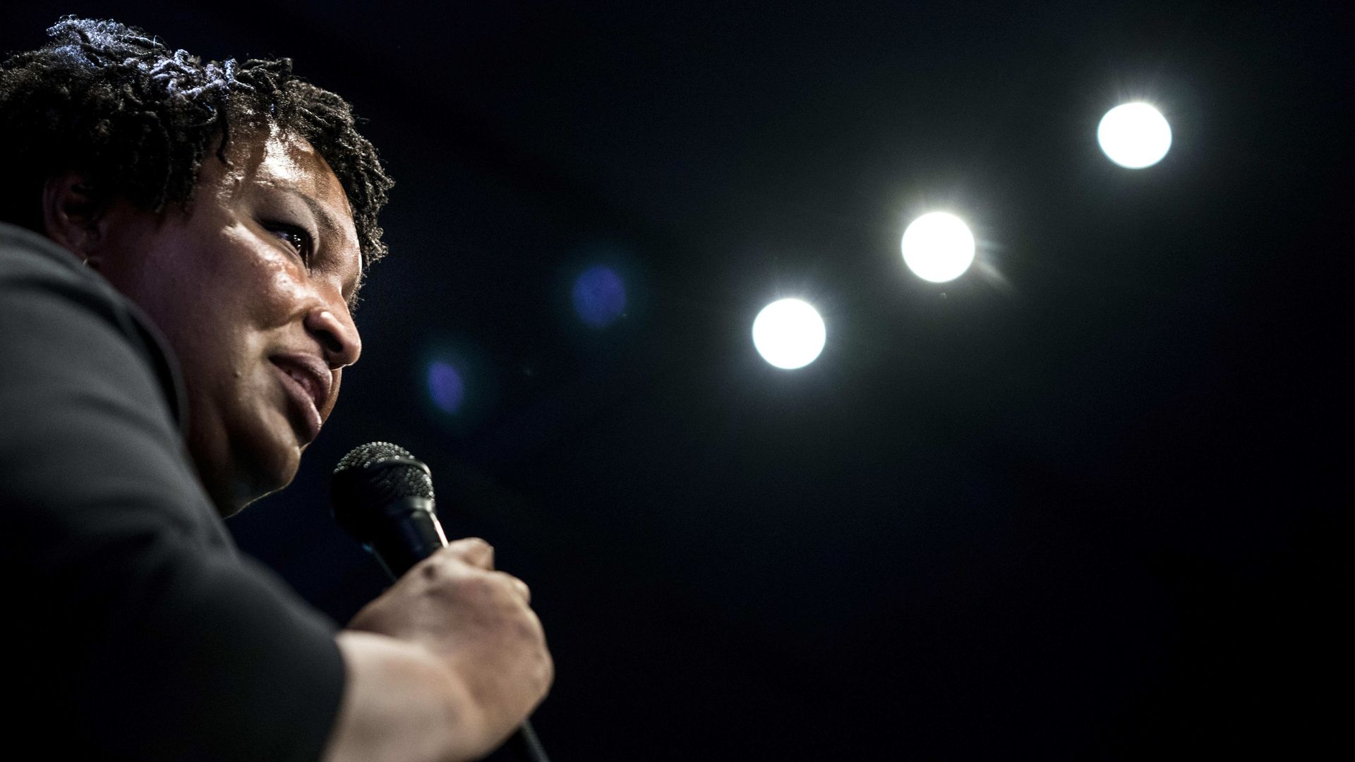 Stacey Abrams speaks into a microphone underneath stage lights. 