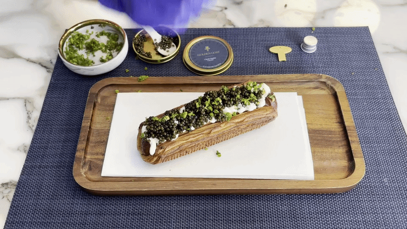 A moving image of someone adding gold flakes to a hotdog topped with caviar. 