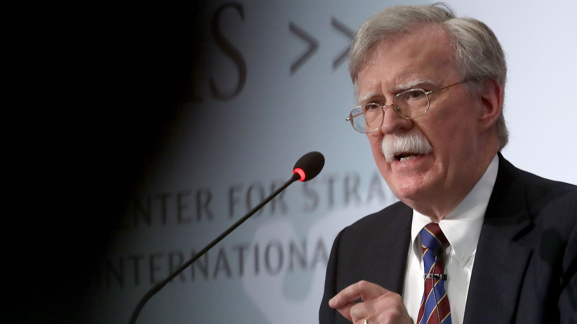 In this image, Bolton speaks into a microphone while wearing glasses.