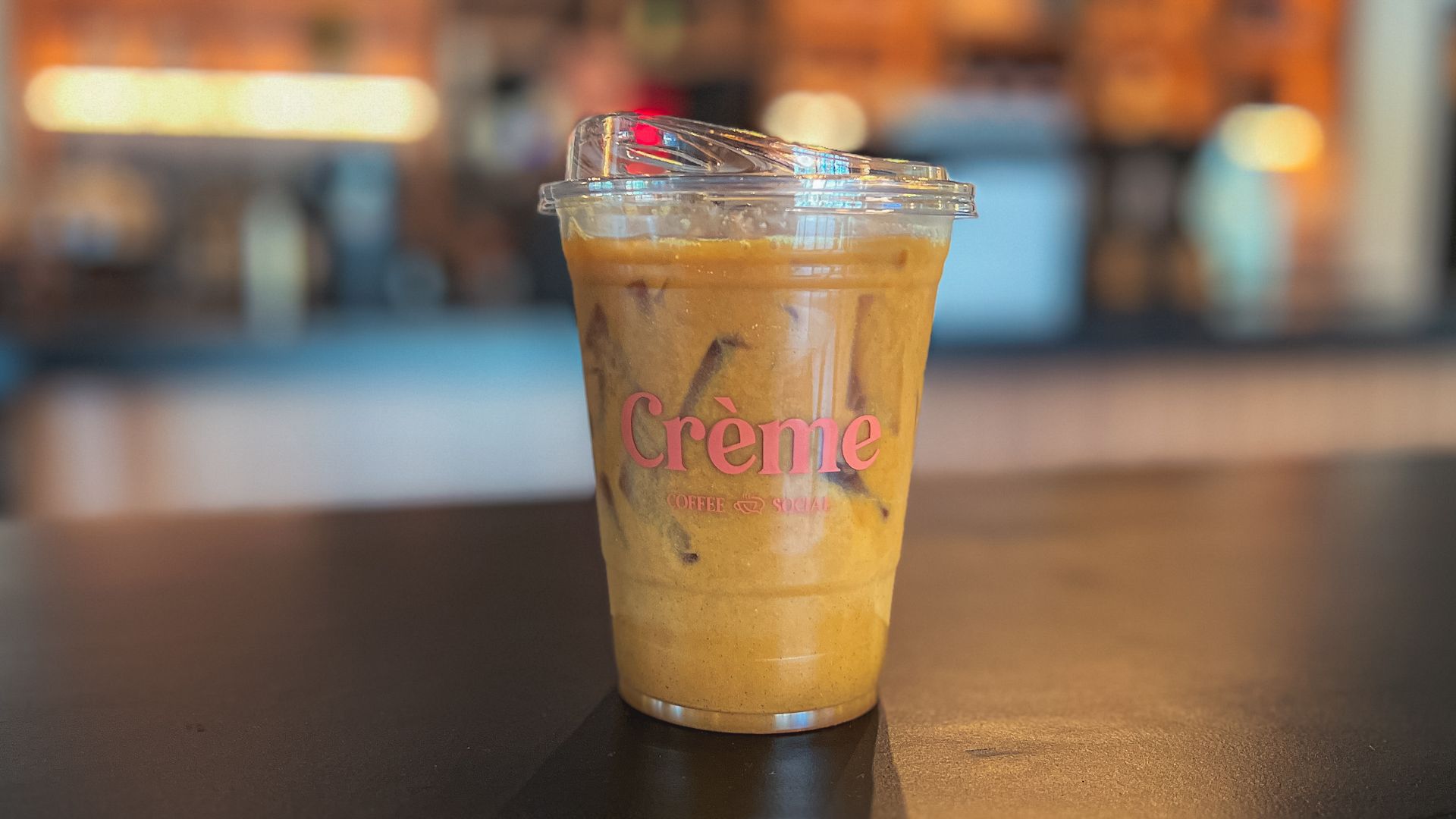 A dirty chai latte in a to-go cup with a pink "Creme" logo, and a blurred coffee shop in the background.