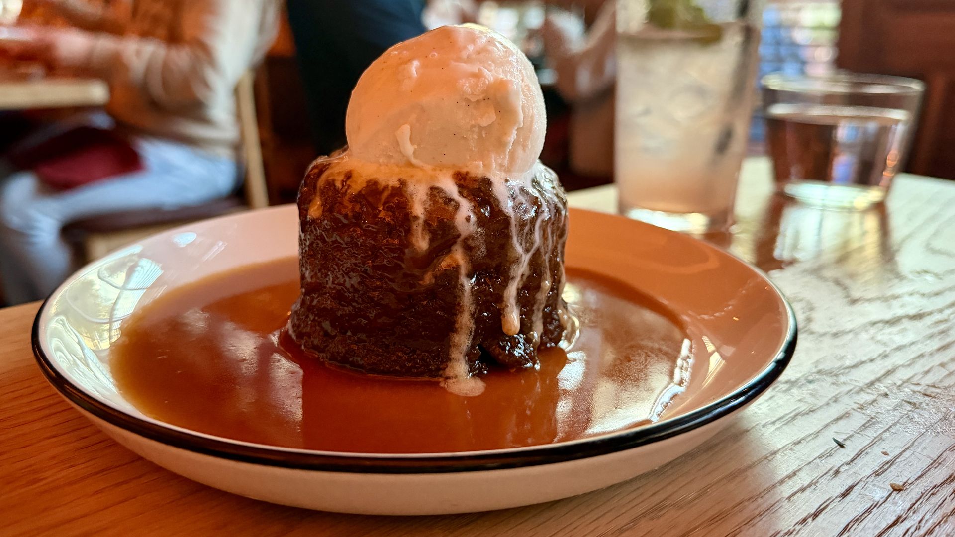 Close-up of a date cake topped with a scoop of vanilla ice cream, drizzled with caramel sauce