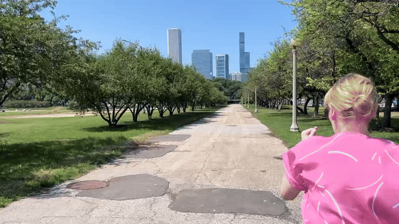 Woman in pink shirt and black pants running down lakefront path. 