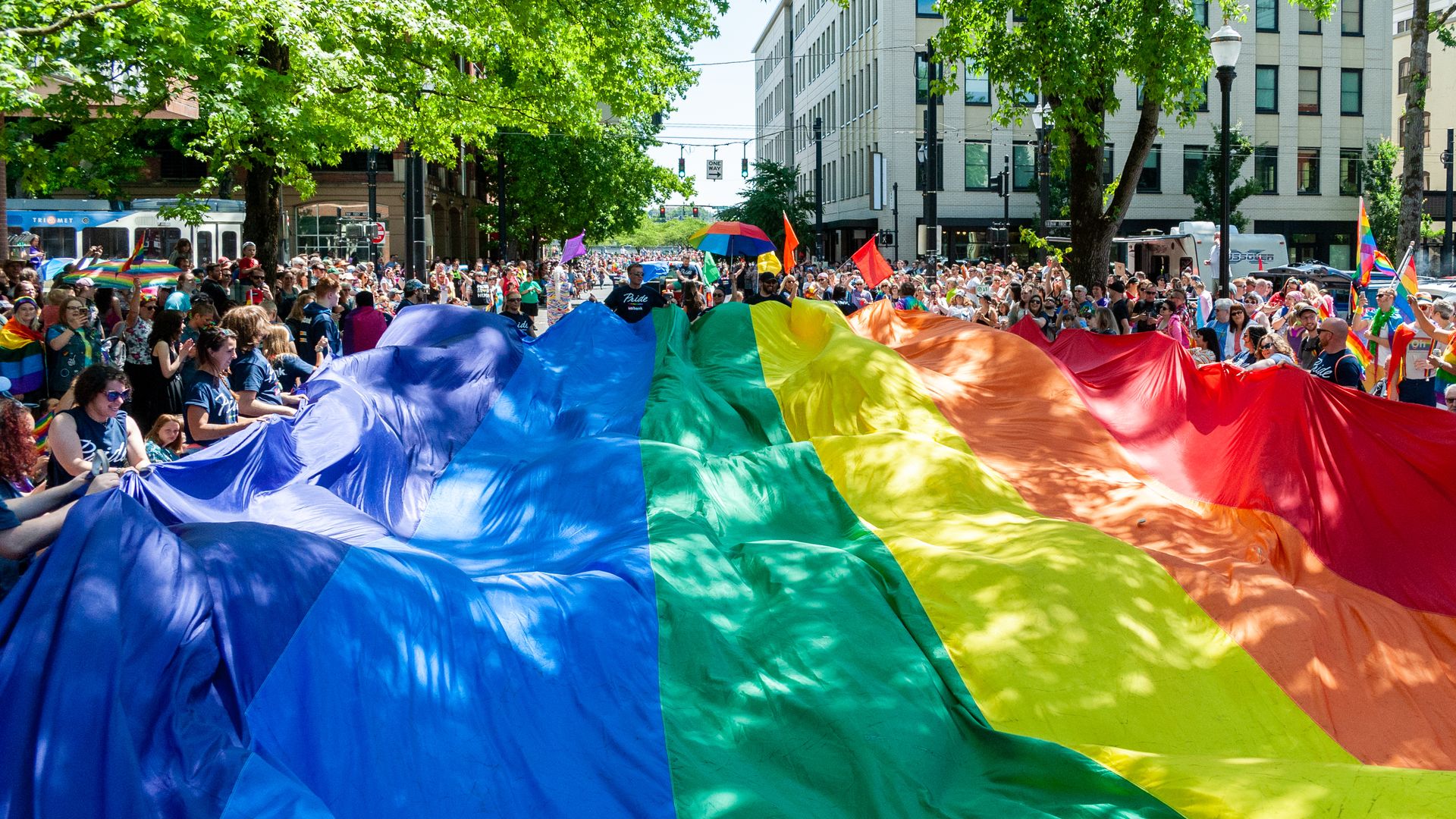 This image shows a large Pride flag being carried down a street.