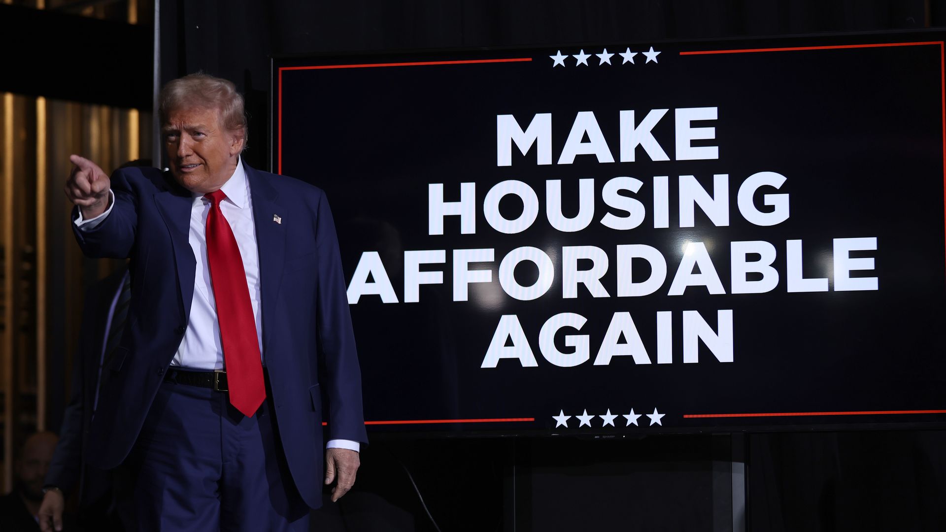 Donald Trump in front of a sign that says, "Make Housing Affordable Again."
