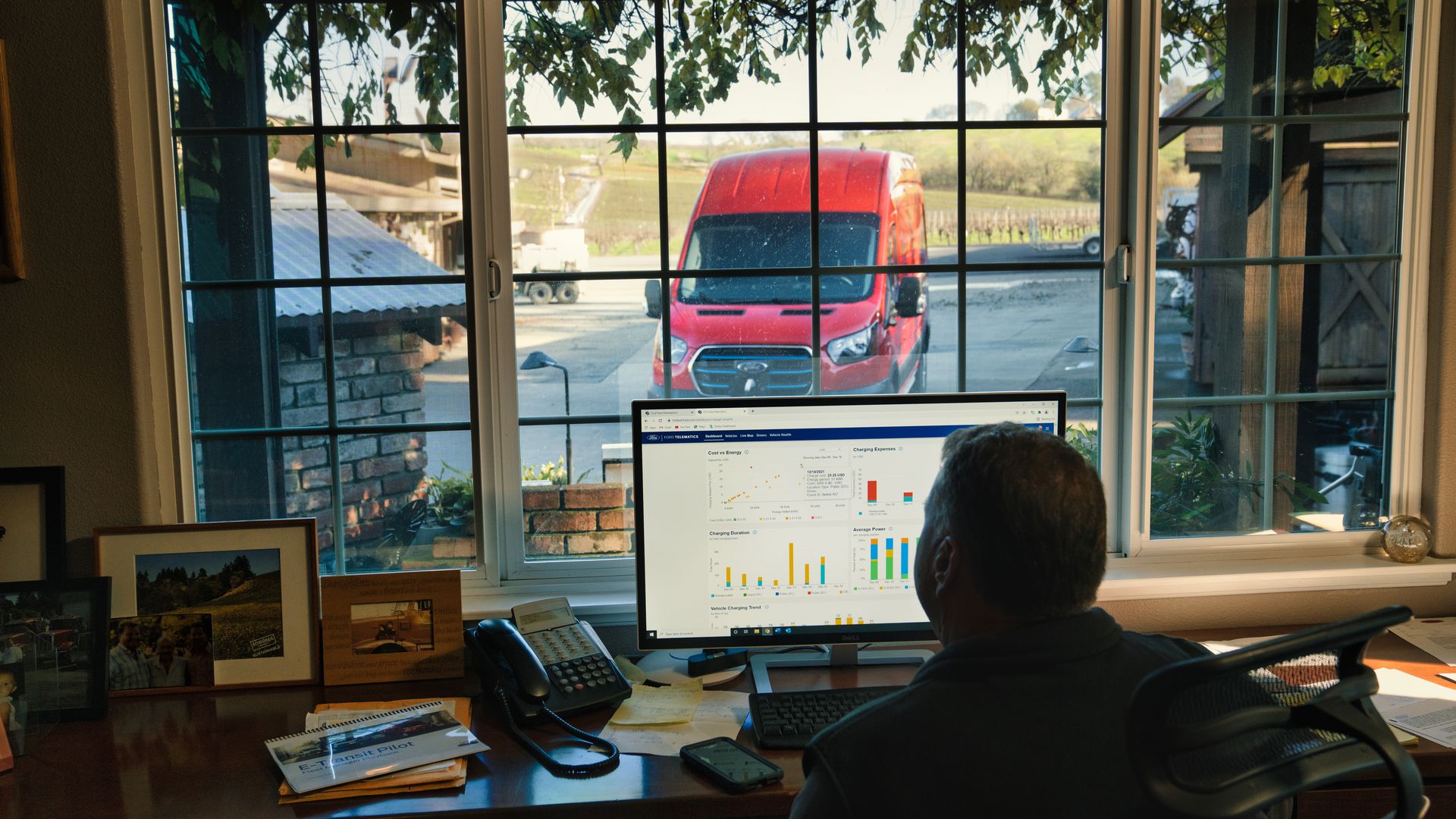 Image of a farmer studying computer data about his electric van, parked outside. 