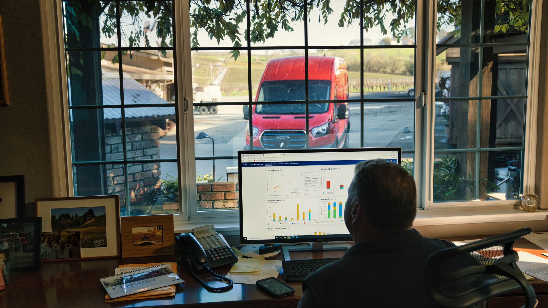 Image of a farmer studying computer data about his electric van, parked outside.