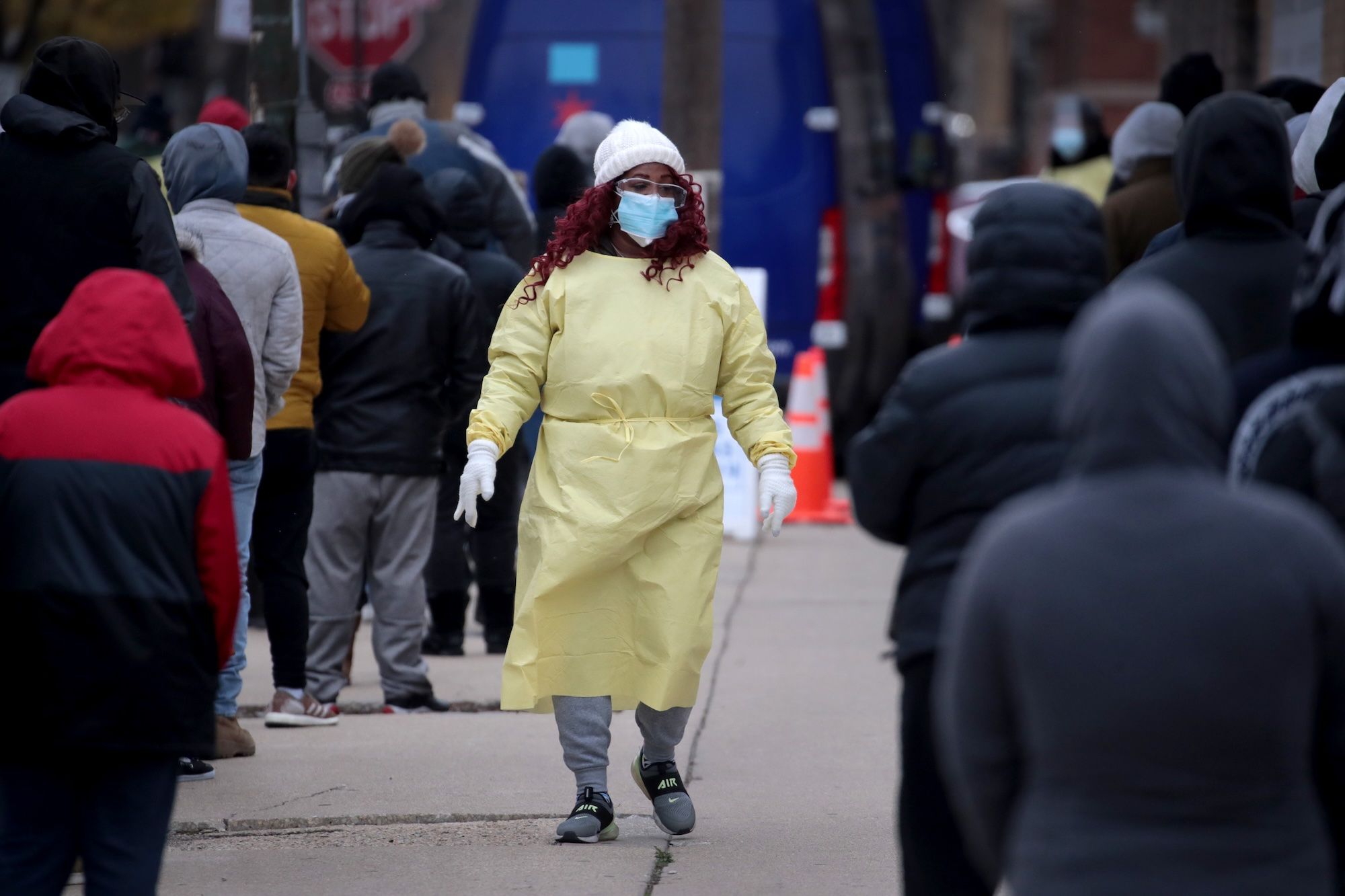 A woman in a hospital gown and medical masks walks through two lines of people.