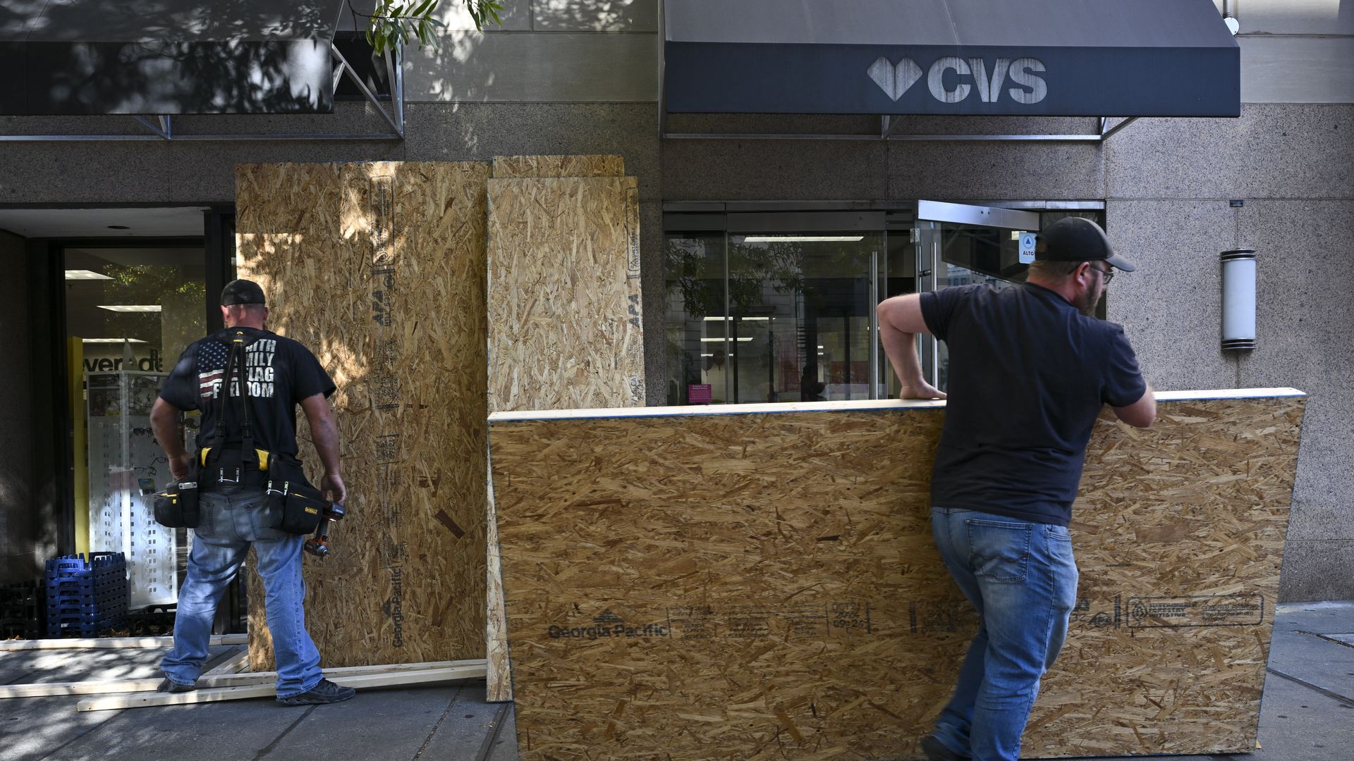 A photo showing two men taking plywood off the windows of a CVS building.
