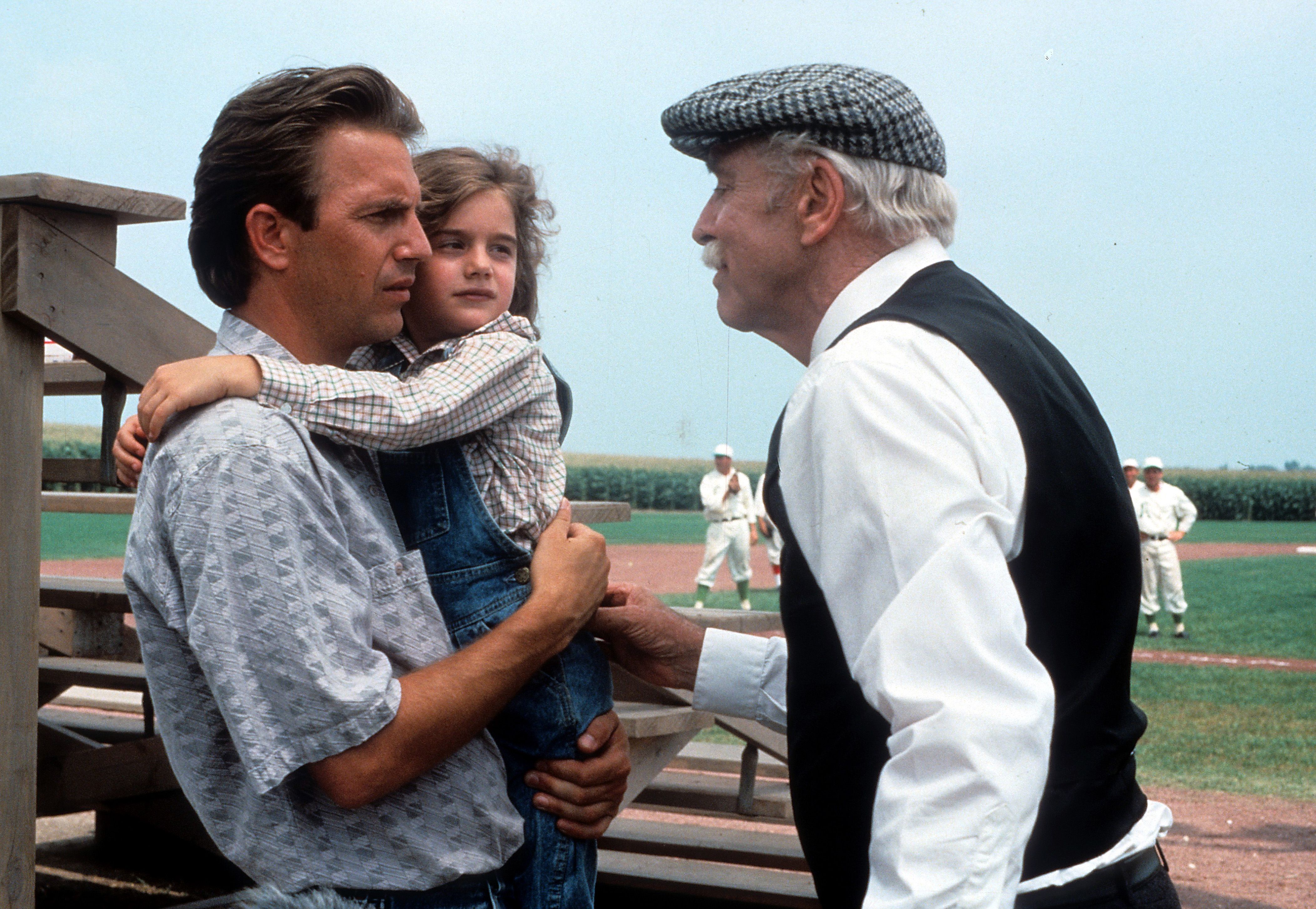 Kevin Costner holding Gaby Hoffmann next to Burt Lancaster in a scene from the film 'Field Of Dreams', 1989. 