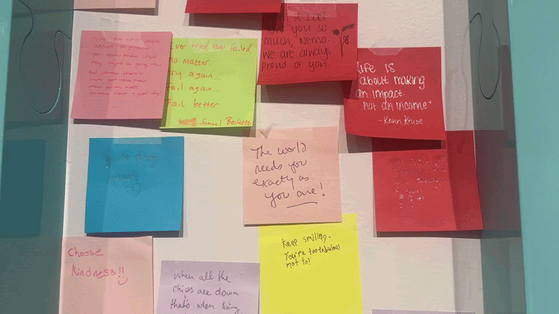 A wall covered with colorful sticky notes—pink, blue, yellow, and green—each with handwritten inspirational messages and quotes in a collage-like display.