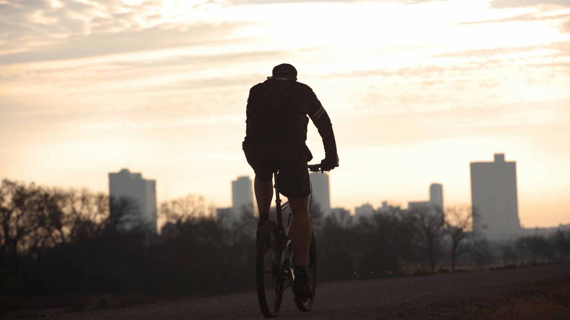 A photo of the back of a person on a bike riding toward the Fort Worth skyline