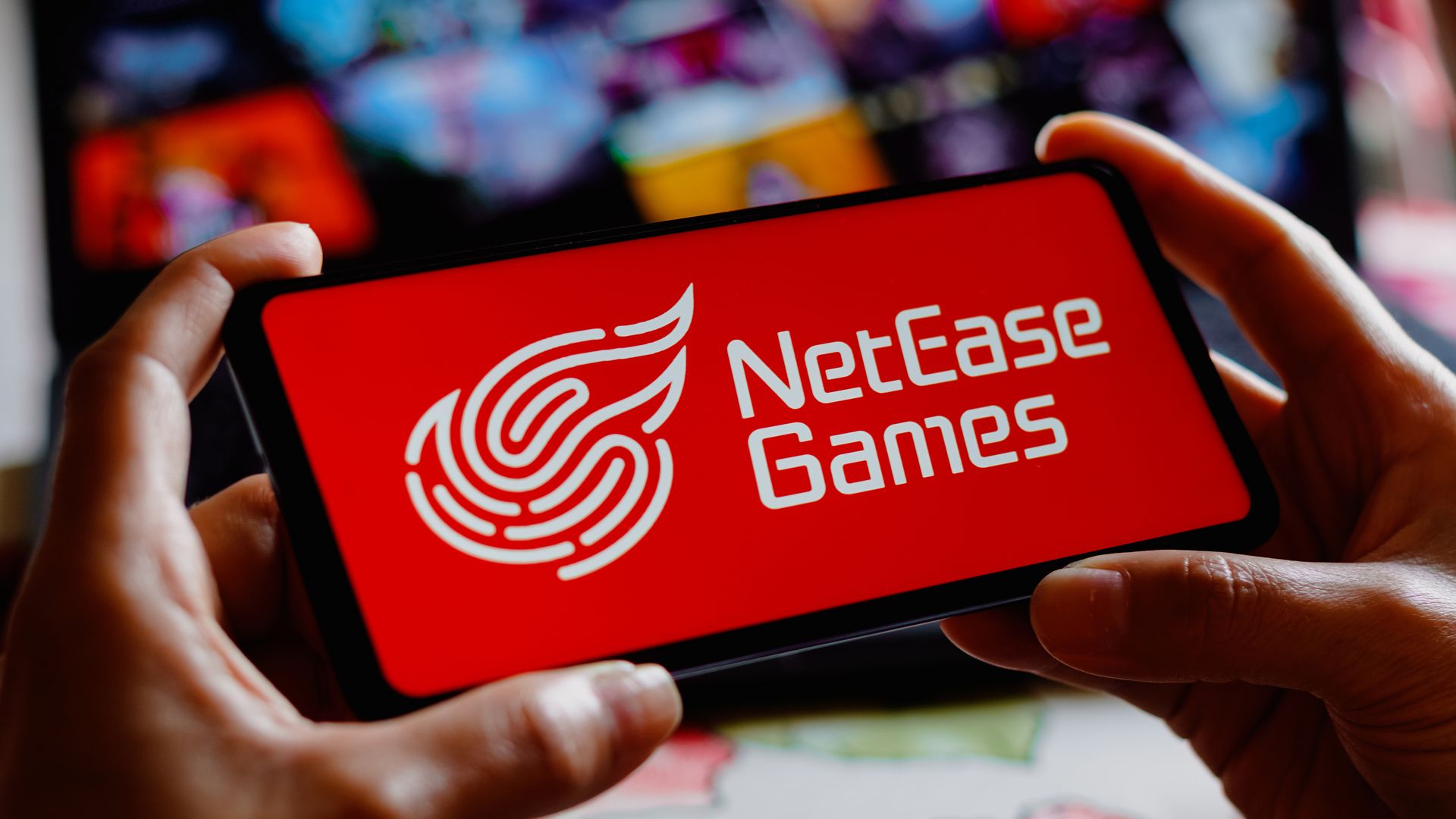 Close-up photo of hands holding  a phone that displays the NetEase Games logo