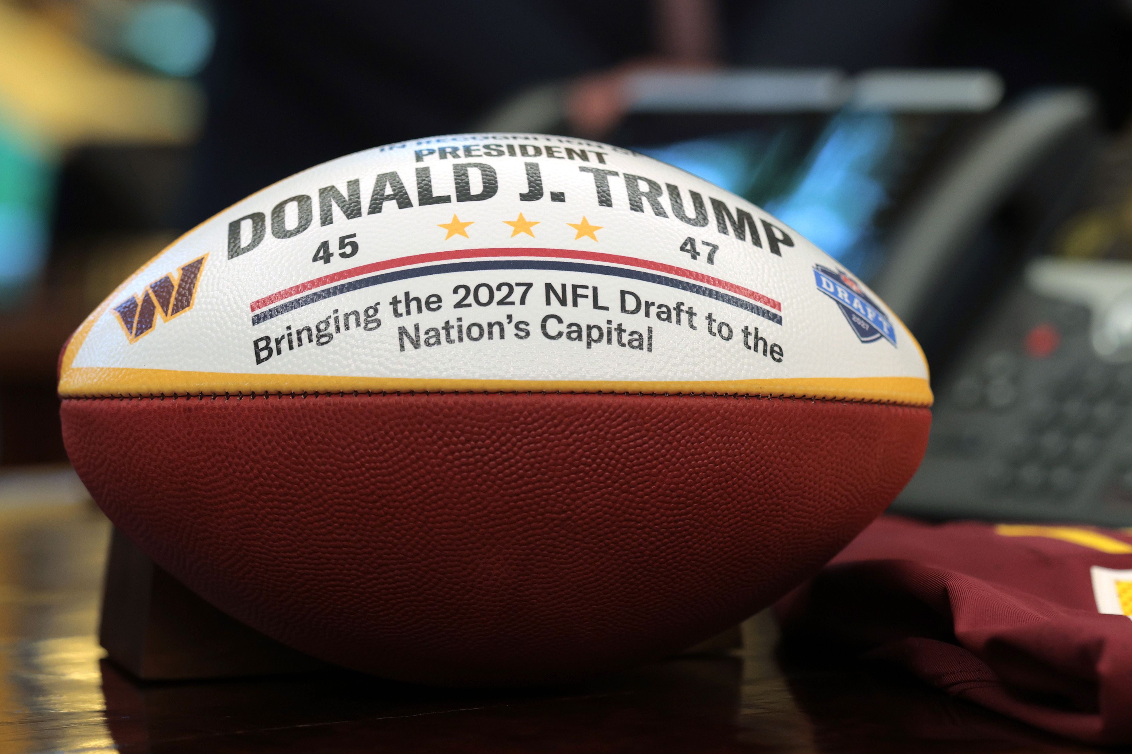 A football honoring President Trump sits on the Resolute Desk during an Oval Office event announcing that the 2027 NFL Draft will be in D.C.