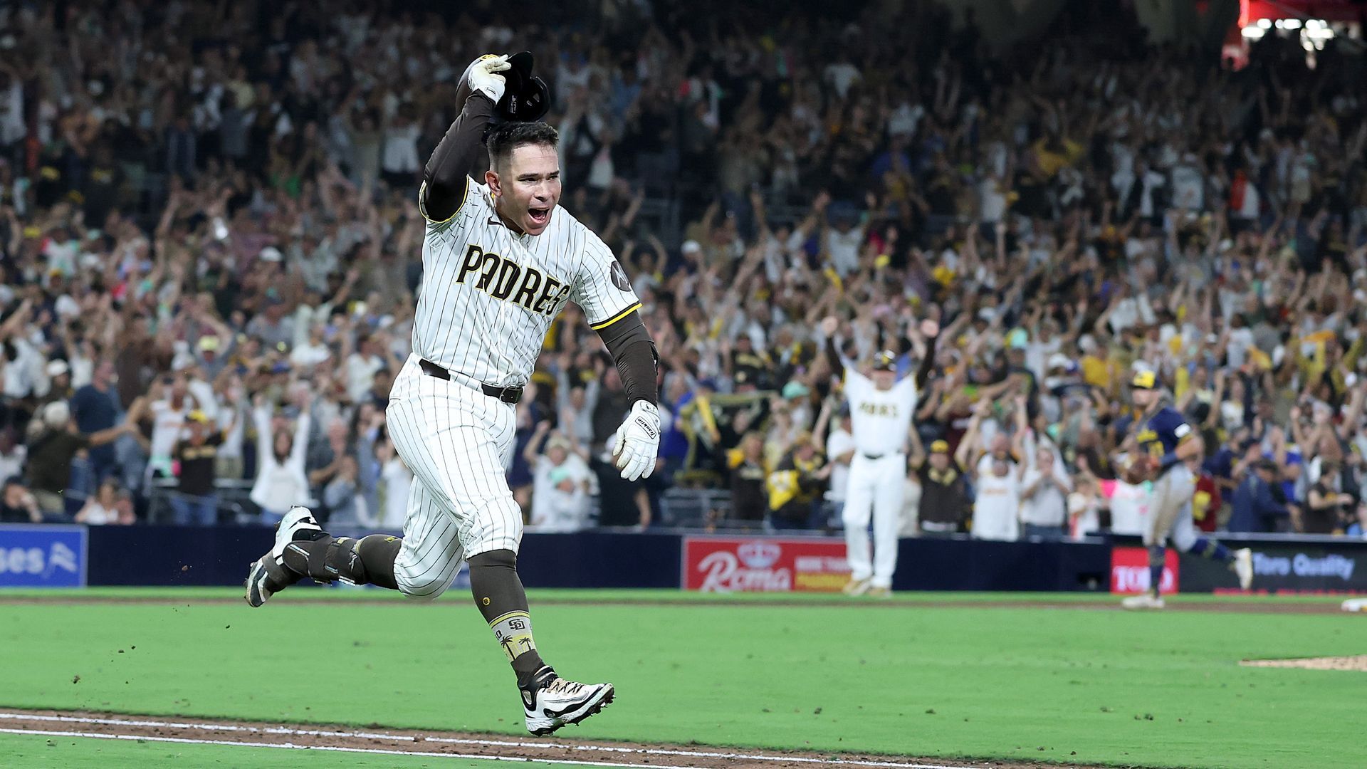 Padres player Freddy Fermin takes his helmet off in celebration while running to first base.