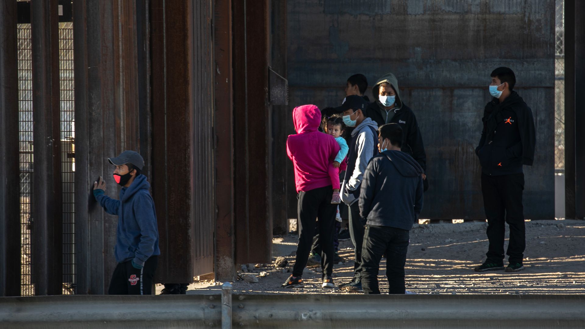 Undocumented immigrants stand next to the border wall while waiting for U.S. Border Patrol agents to arrive 